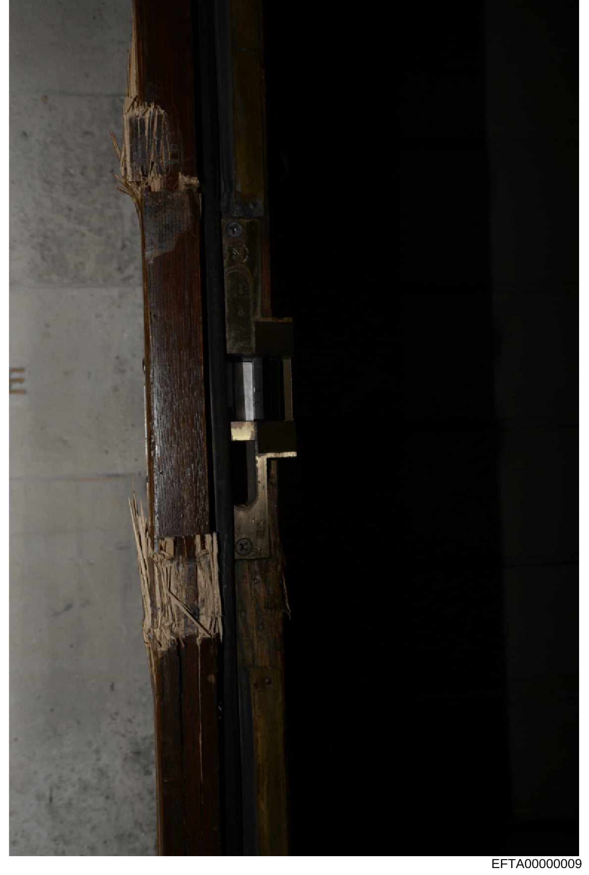 This is an evidence photograph showing a close-up detail of a wooden door frame with visible damage to the wood and what appears to be a brass or metal lock mechanism. The image appears to be from a property inspection or forensic documentation, like