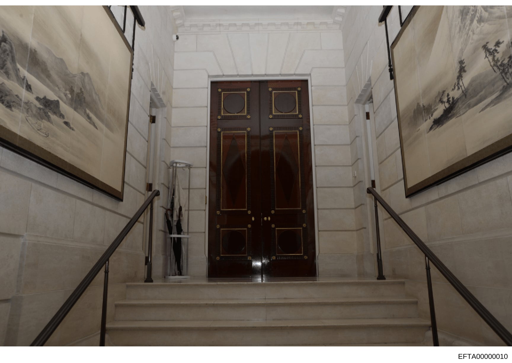 This is an evidence photograph showing the interior of a formal building or residence, specifically a staircase leading to an impressive pair of dark wood double doors with brass hardware and inlay work. The image documents architectural features of