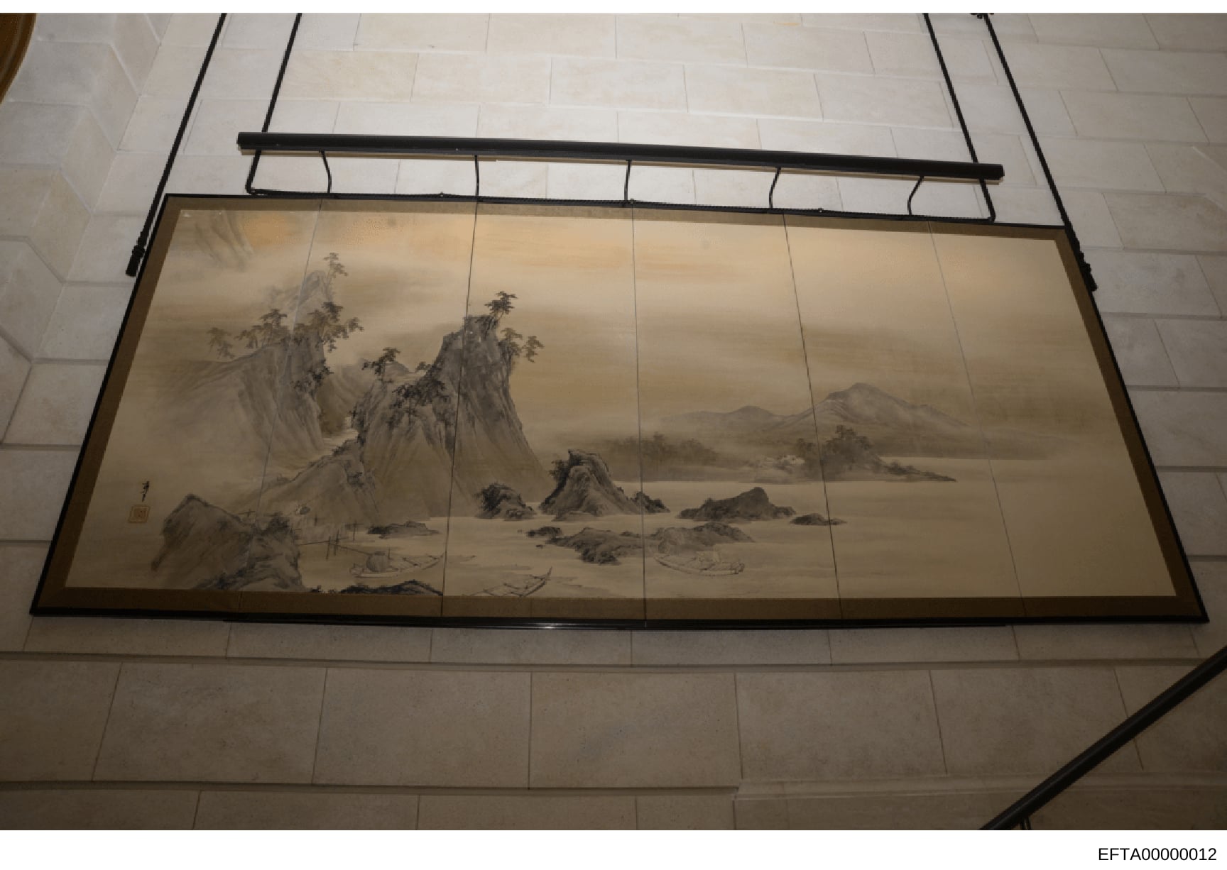 This photograph shows a framed traditional Asian landscape artwork installed on a ceiling, featuring a monochromatic mountainous scene with water, rocks, and sparse vegetation in classical ink painting style. The artwork is mounted in a black-framed 