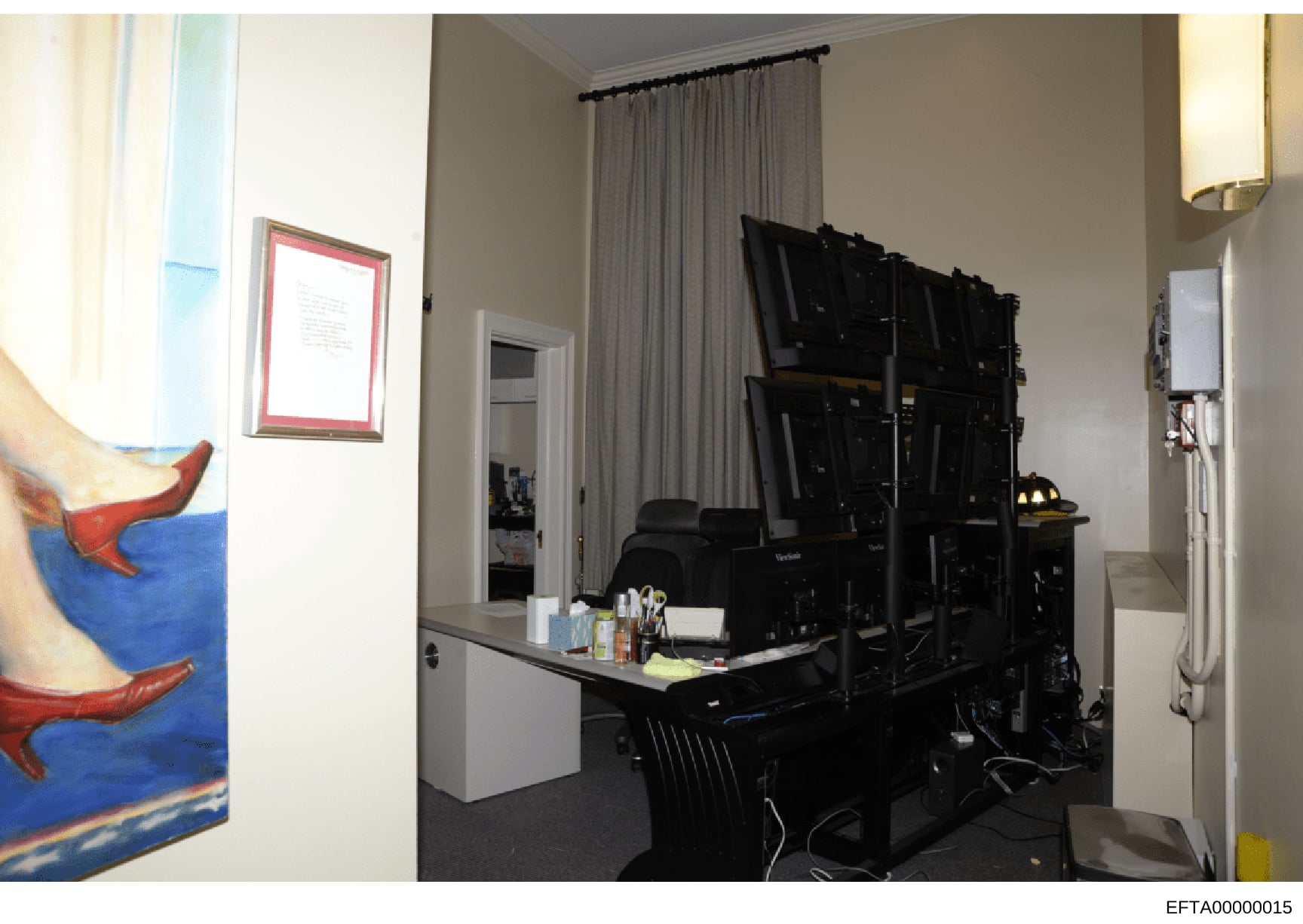 This photograph shows an interior room containing computer equipment, multiple monitors mounted on a wall, and office/workspace furniture. The room appears to be part of a residential property with modern amenities, including curtained windows, artwo