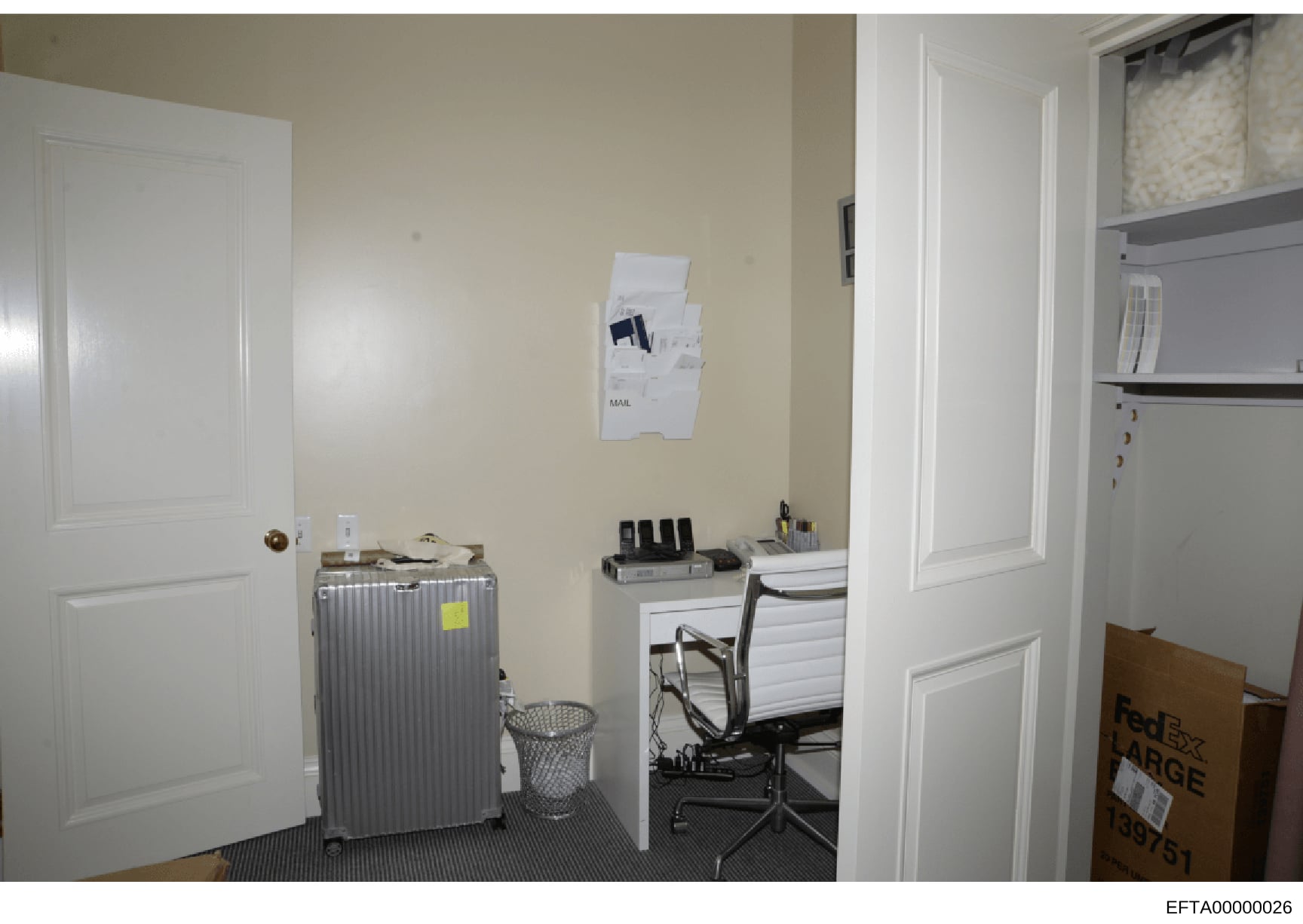 This is an evidence photograph showing an interior office or workspace room. The image captures a desk area with computer equipment, filing cabinets, a mesh trash bin, wall-mounted mail organizer, shelving units, and various office supplies. A FedEx