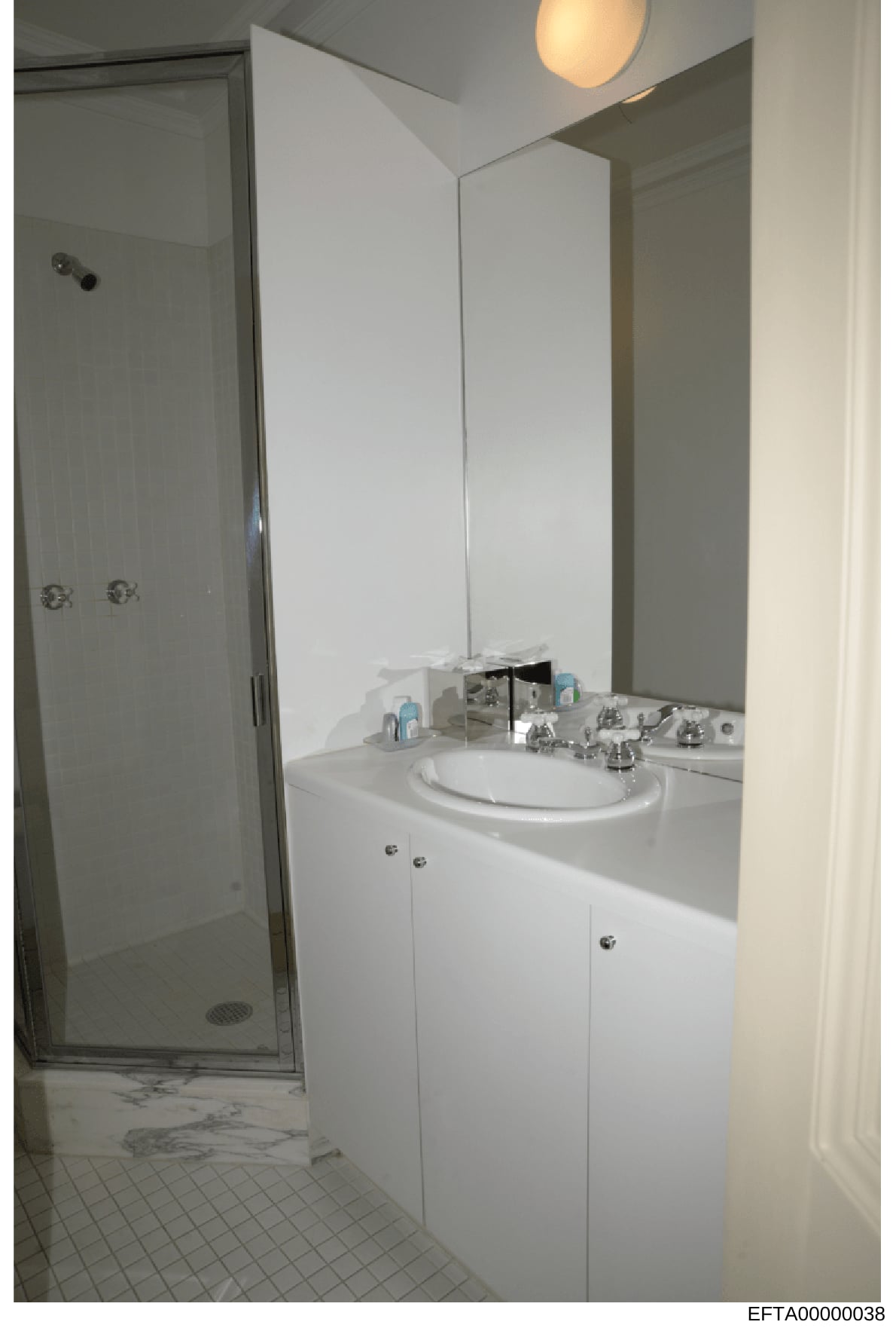 This is a photograph of a modern bathroom interior, showing a white vanity with a round sink, large mirror, and glass shower enclosure. The image appears to be evidence documentation from a property investigation, capturing the bathroom fixtures and 