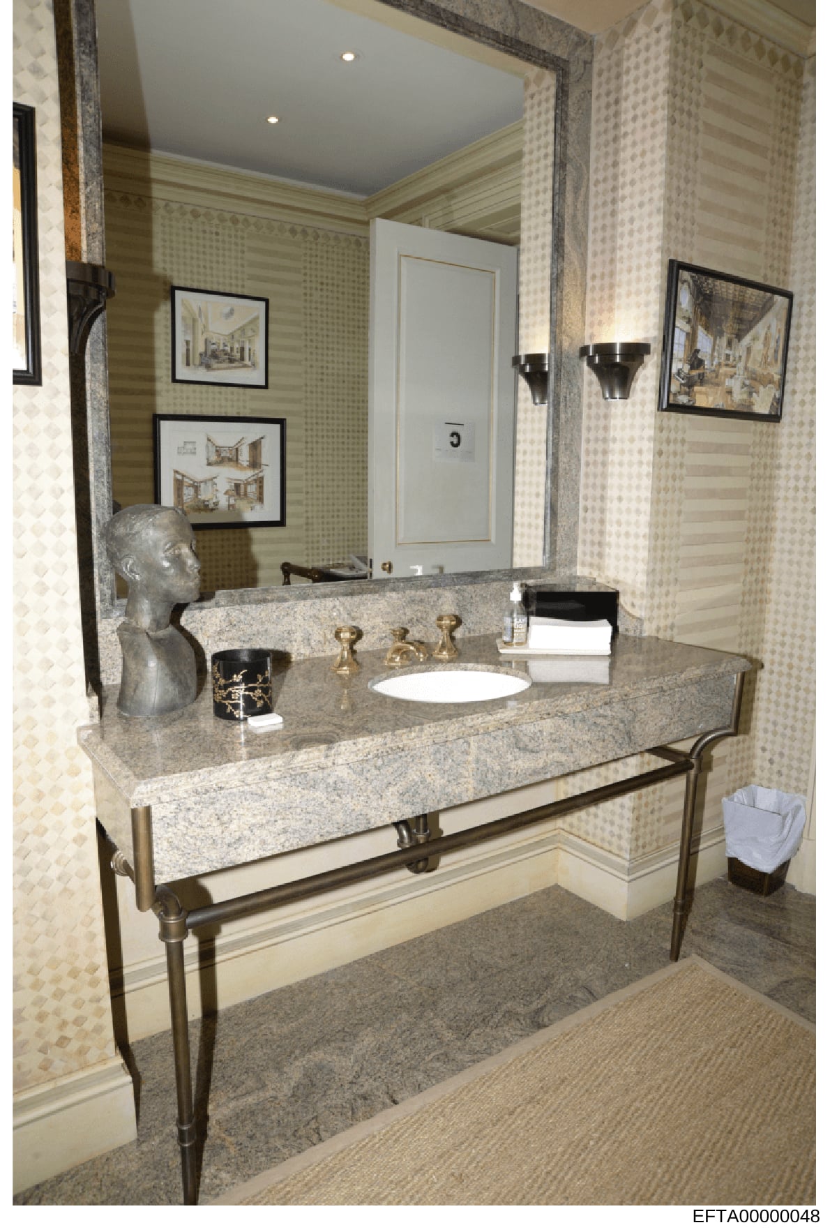 This is a photograph of a luxury bathroom interior featuring a double granite vanity with brass fixtures, decorative bust sculpture, framed architectural prints, and custom wall coverings. The image appears to be from a property inventory or real est