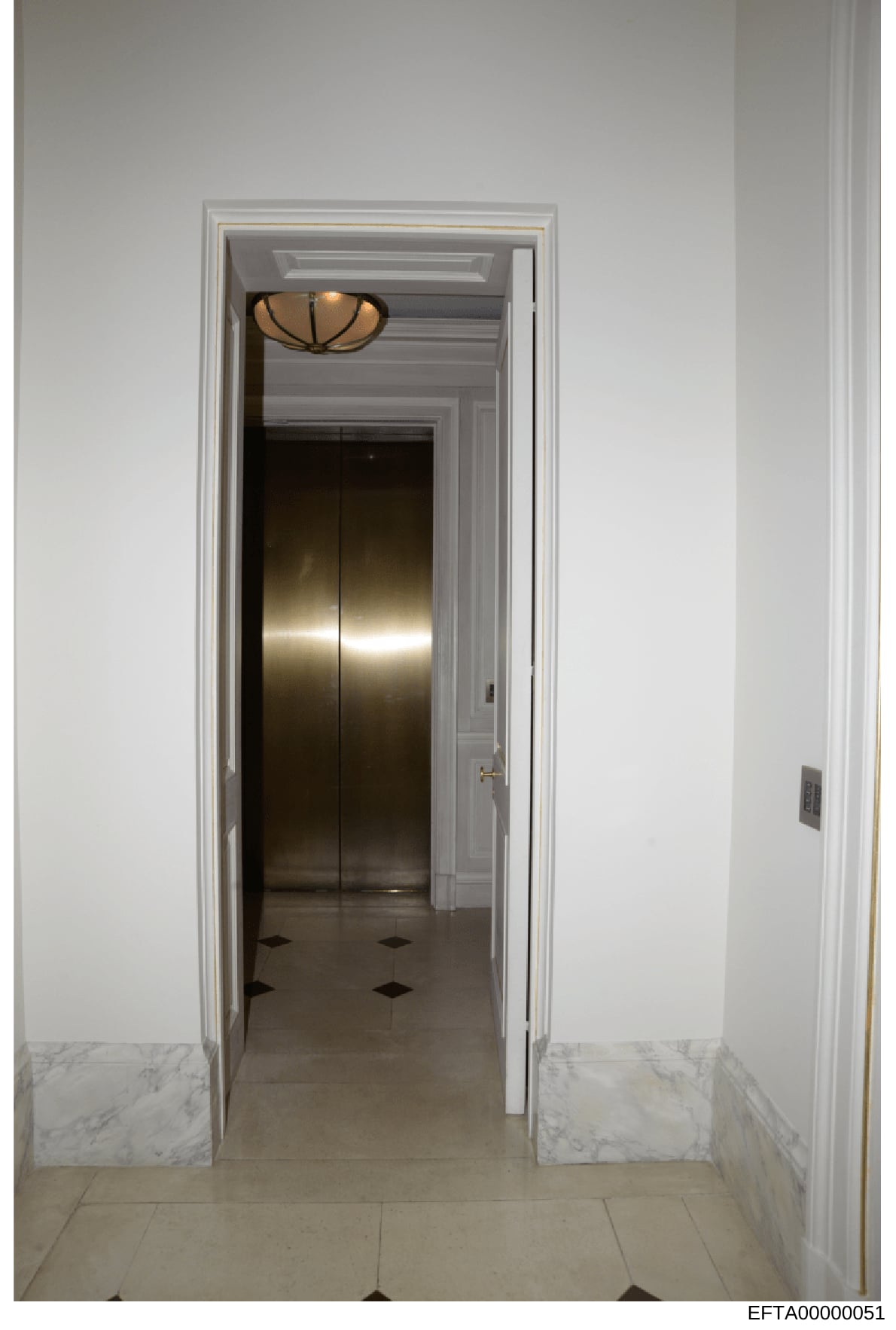 This photograph shows a modern hallway interior with an elevator entrance, marble wainscoting, and decorative ceiling fixture. The image appears to be evidence documentation of a property associated with the investigation, showing architectural detai