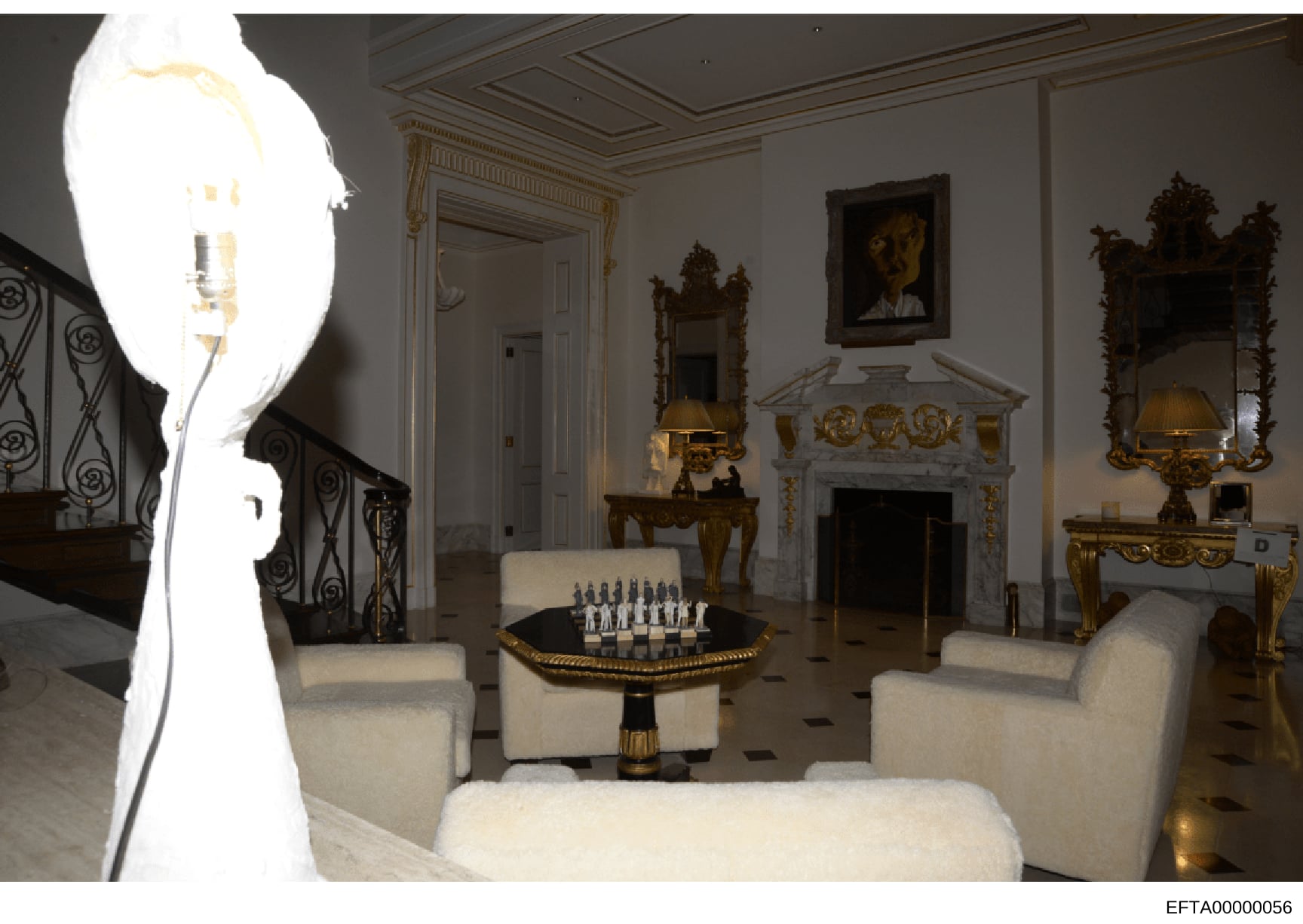 This is a photograph of an ornately decorated formal living room featuring neoclassical and baroque-style furnishings, including gilded mirrors, marble fireplace, decorative sculptures, and cream-colored upholstered seating. A chess set is displayed