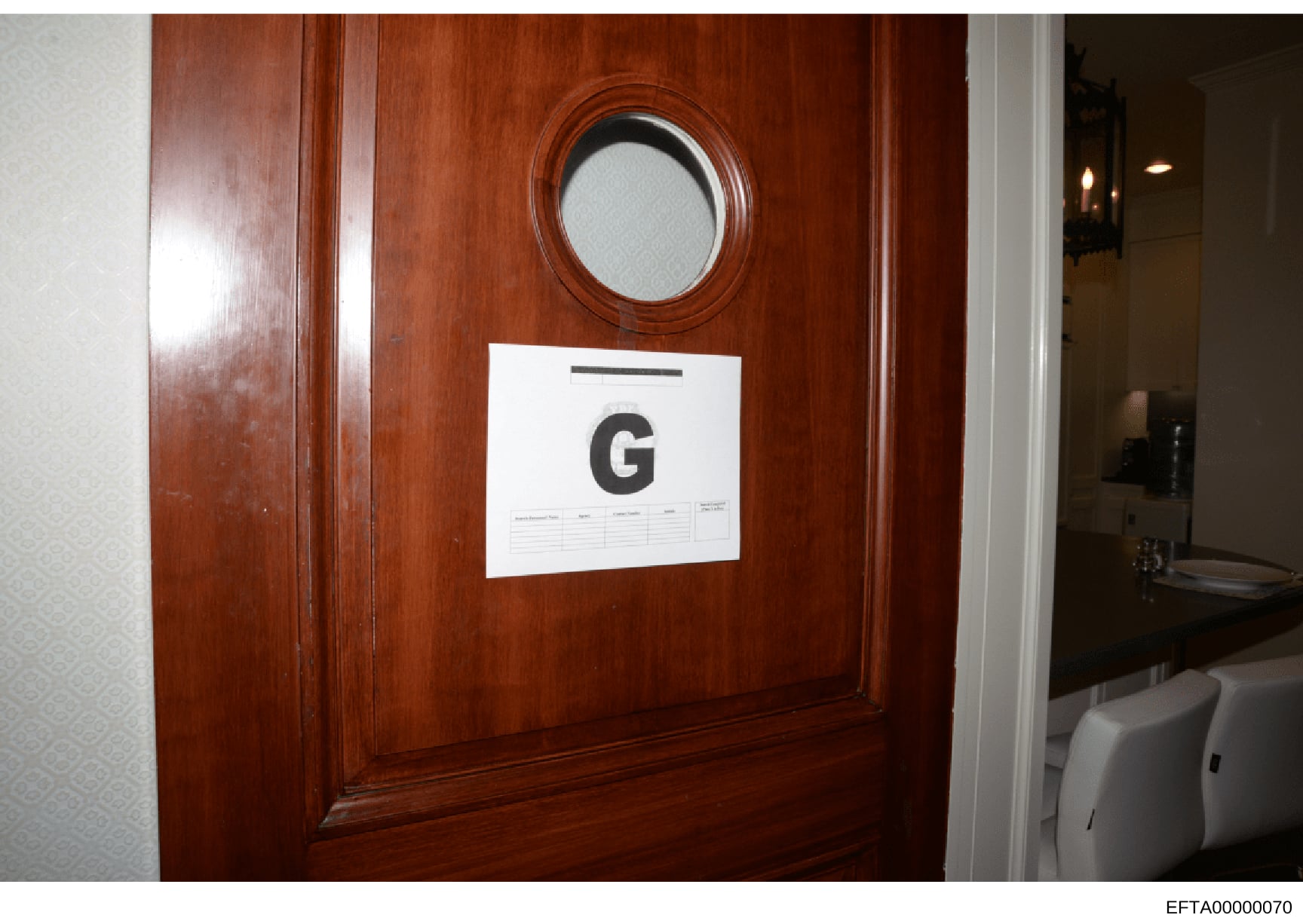 This is a photograph of a wooden door marked with evidence marker 'G' during an investigation. The door features a circular porthole window and ornate wood framing. The white evidence placard indicates this door was photographed and cataloged as part