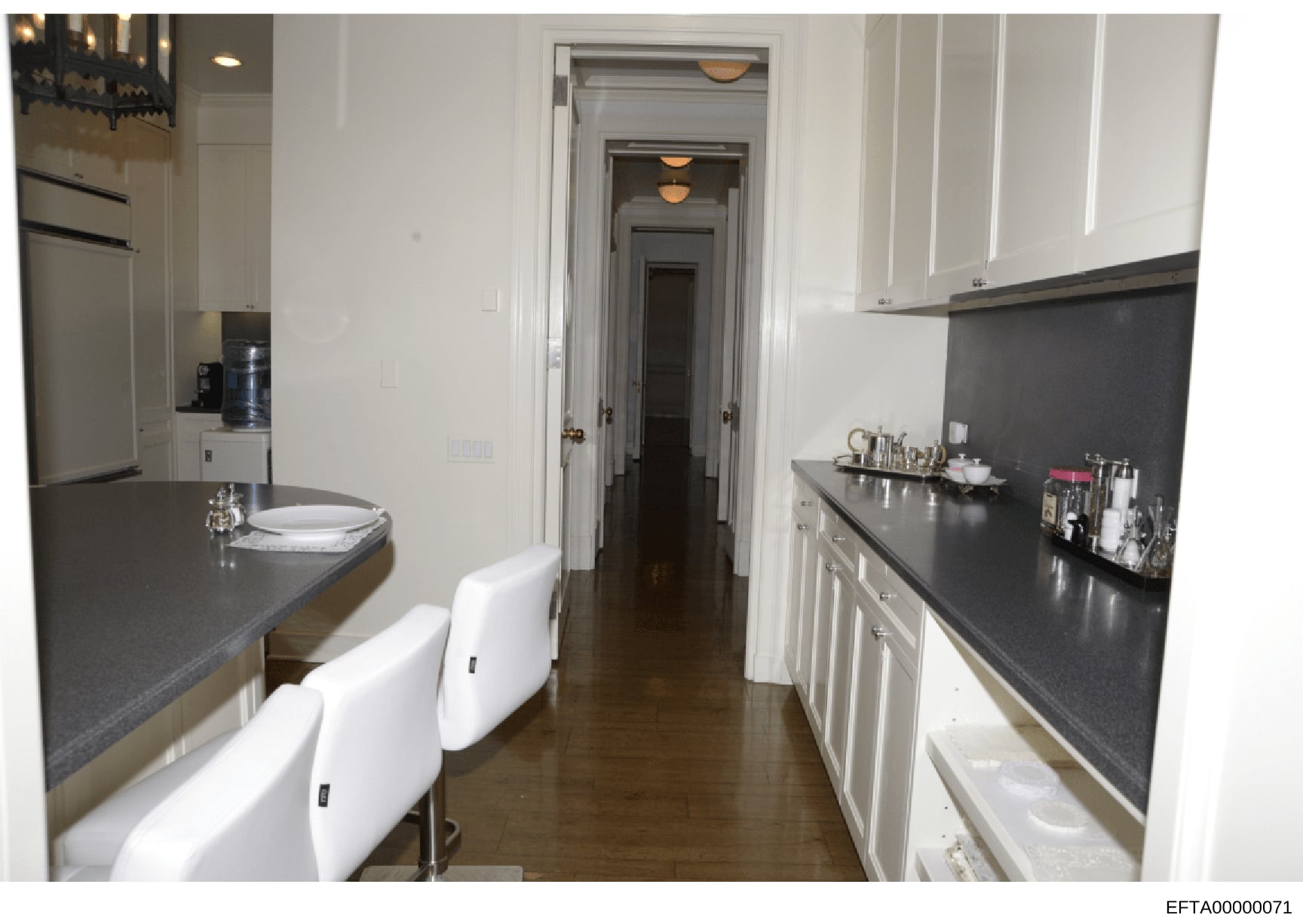 This photograph shows a modern kitchen interior with white cabinetry, dark granite countertops, and stainless steel appliances. The image appears to be from an inventory or property documentation, showing a galley-style kitchen layout with two seatin