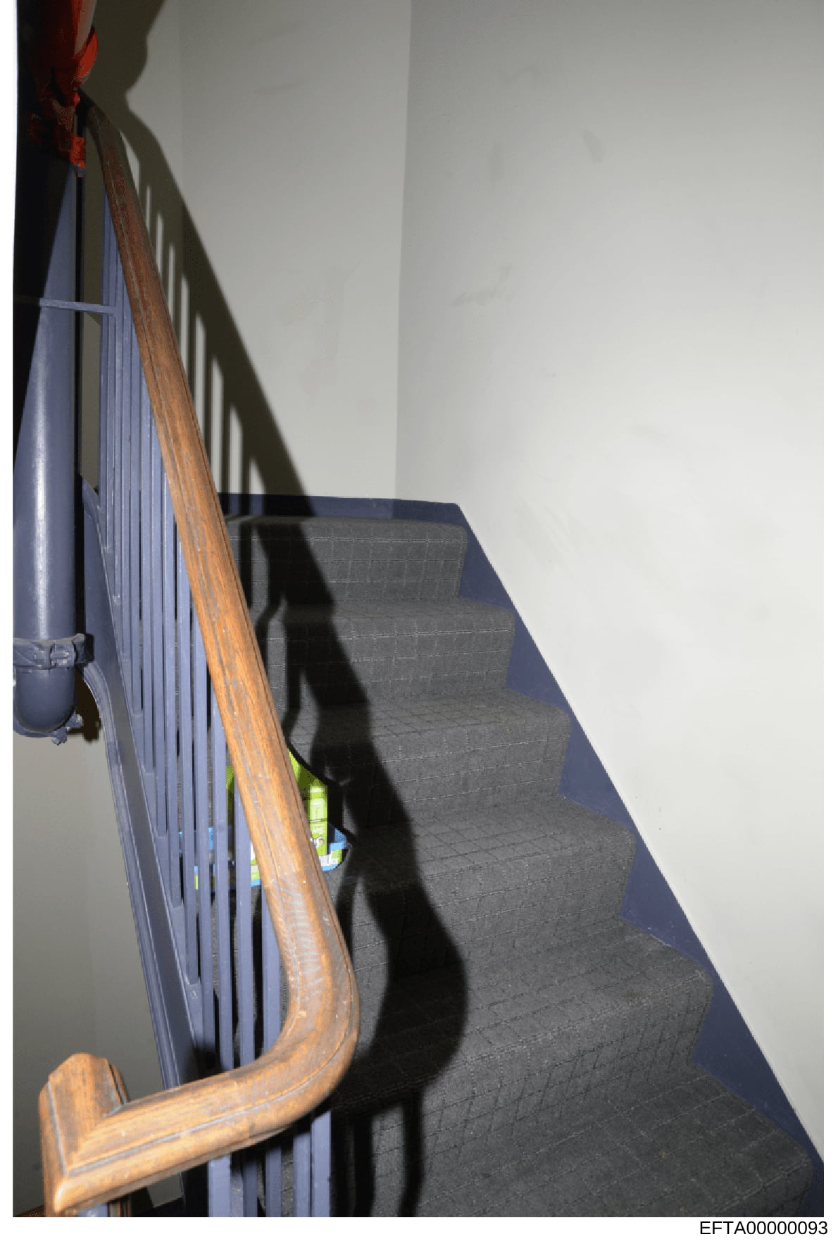 This is a photograph of an interior staircase featuring a wooden handrail with a polished finish and a blue/purple metal railing with vertical spindles. The image captures architectural details of what appears to be a residential property, with white
