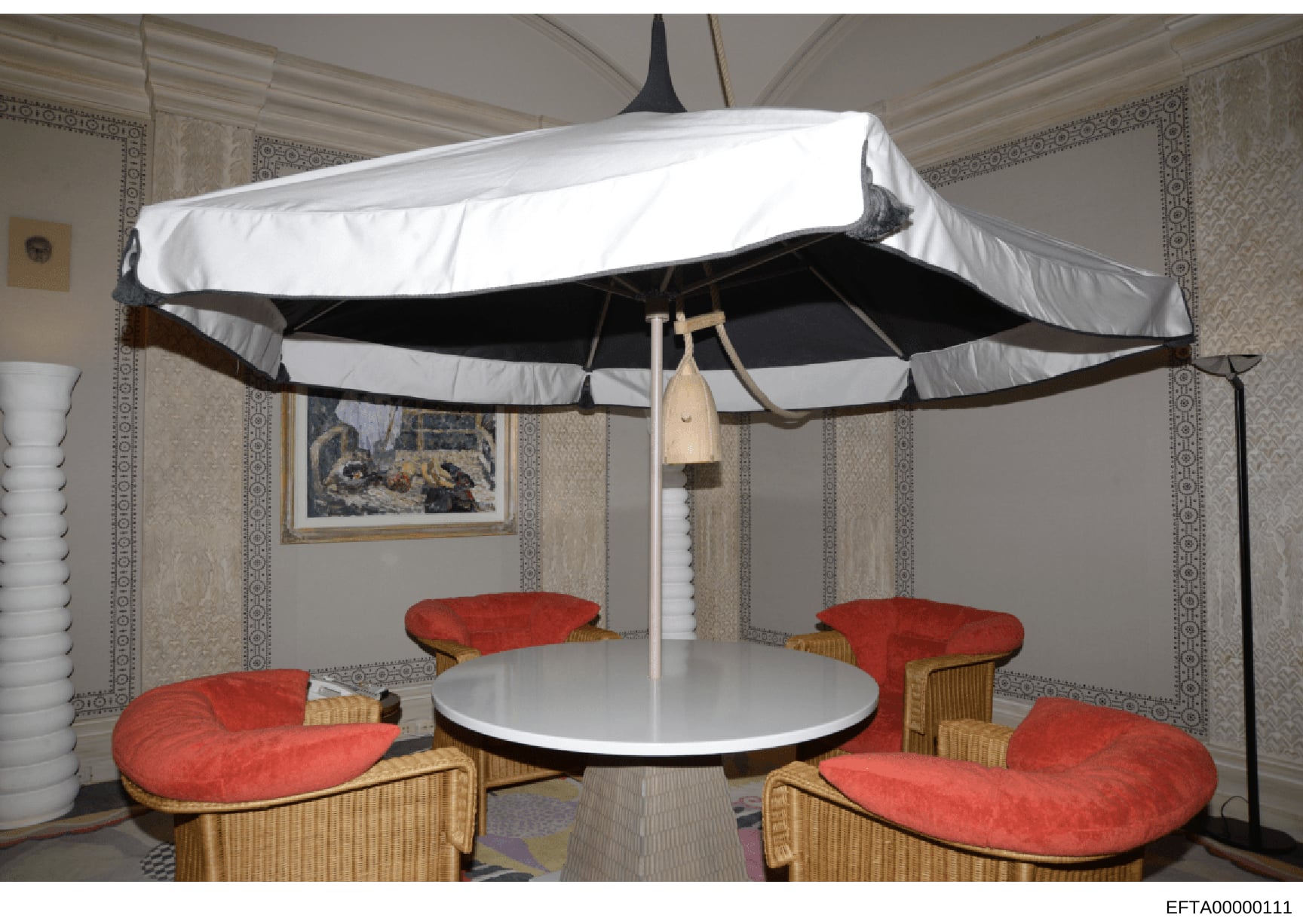This photograph shows a high-end interior space featuring a large circular white and black striped canopy or tent structure with red cushioned seating arranged around a white circular table. The space displays sophisticated furnishings including wick