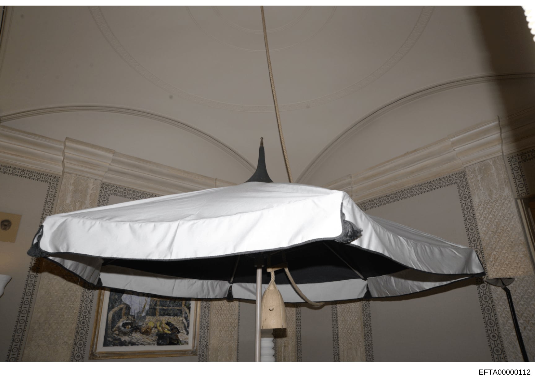 Evidence photograph showing a decorative airplane model suspended from the ceiling of an interior room. The model features white and black coloring and appears to be a vintage or mid-century design. The photograph documents the interior décor of what