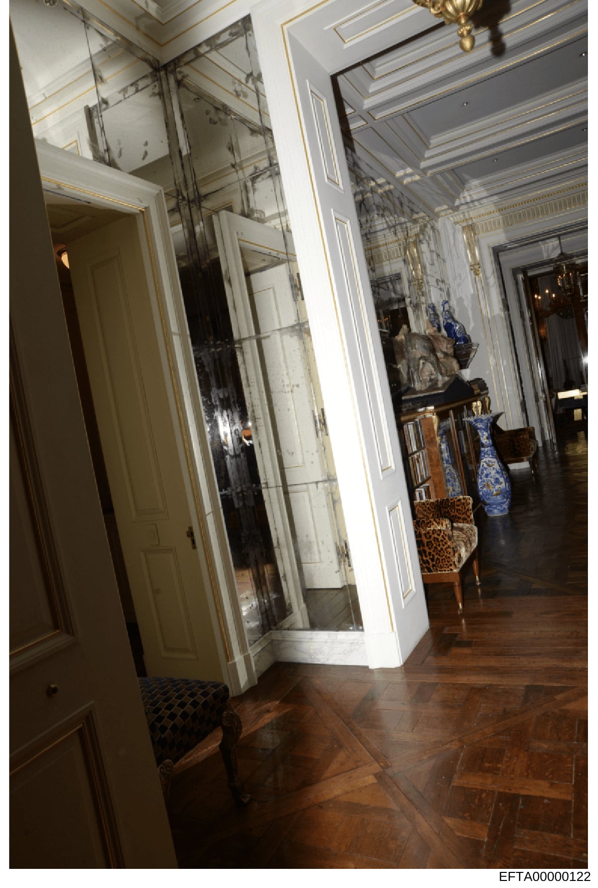 This photograph shows an elegant interior hallway, likely from one of Epstein's residences, featuring ornate ceiling details, large mirrors, hardwood flooring, and decorative items including blue and white porcelain vases and upholstered furniture. T