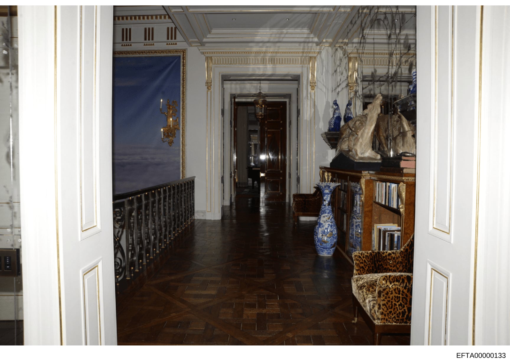 This photograph documents the interior of a hallway in what appears to be a luxury residential property, featuring elegant architectural details, fine furnishings, and decorative items. The image shows a long corridor with white walls trimmed in gold
