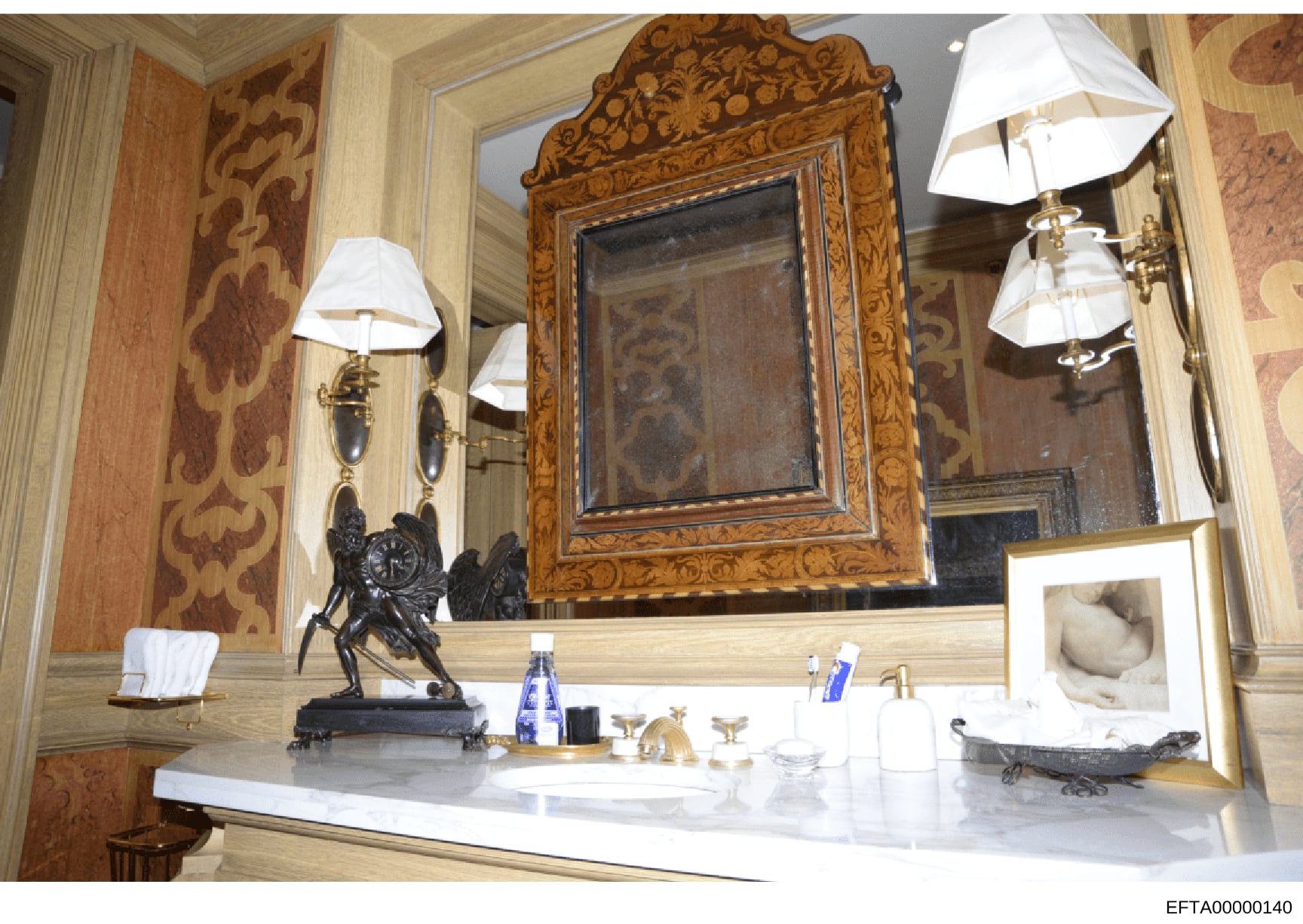 This is a photograph of an upscale bathroom interior featuring an ornate wooden-framed mirror, elegant vanity counter with marble or stone surface, decorative lighting fixtures, and luxury furnishings. The image documents the interior design and déco