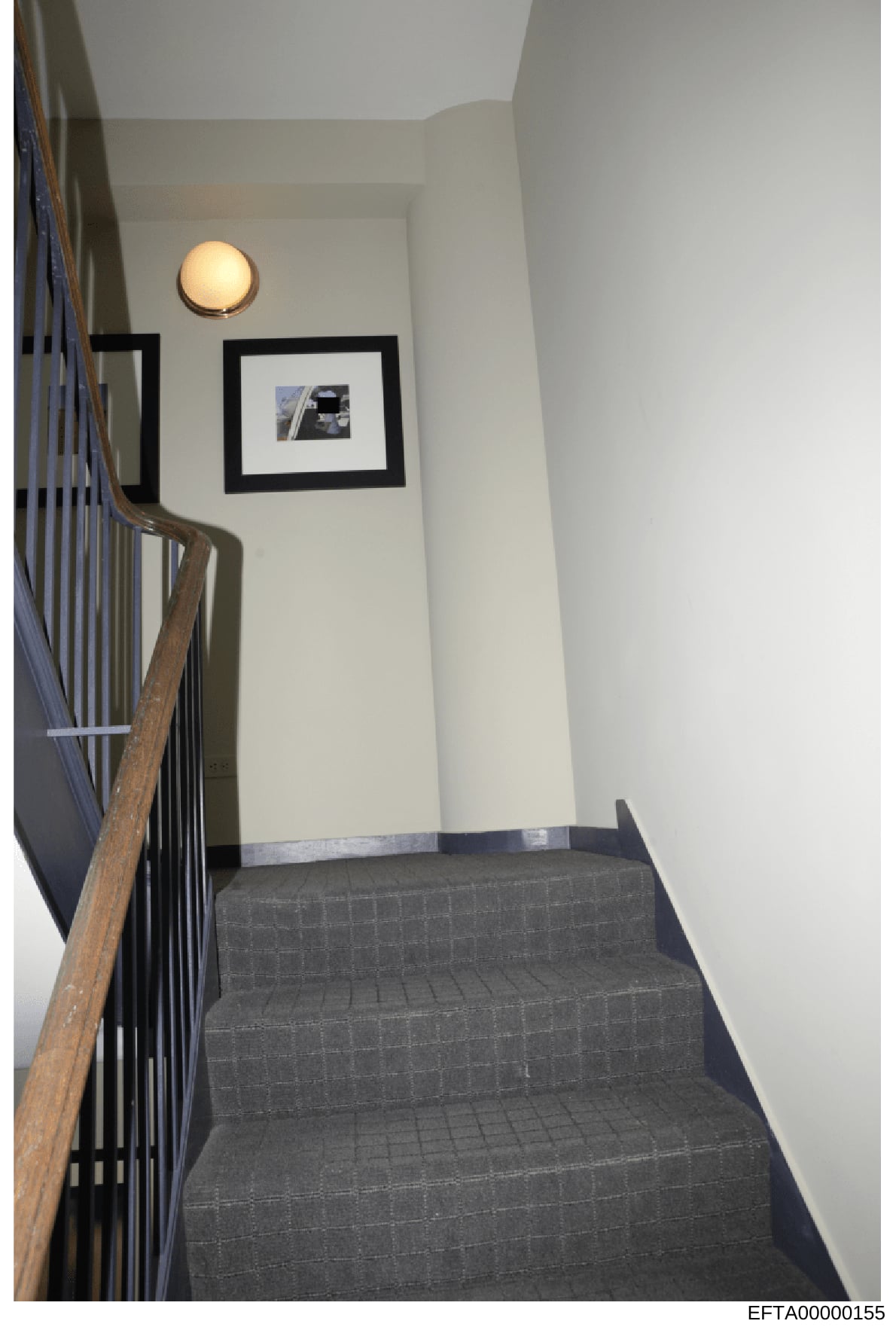 This photograph shows an interior stairwell and hallway from an Epstein property, featuring a modern architectural design with white walls, black-framed artwork, wooden railings, and contemporary lighting fixtures. The image appears to be evidence do