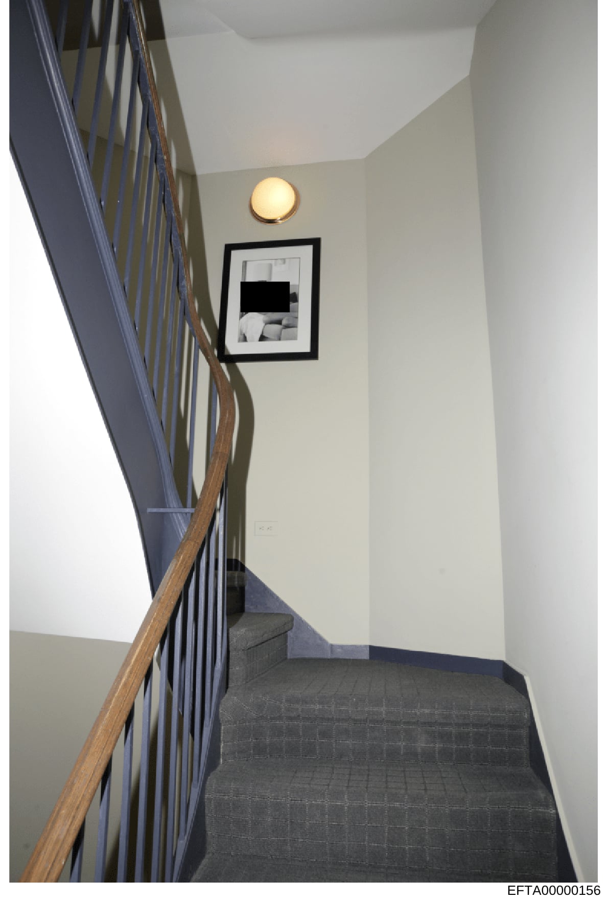This is a photograph of an interior stairwell, likely from one of Jeffrey Epstein's properties, showing architectural details including a metal railing with wooden handrail, cream-colored walls, recessed lighting, and a framed artwork on the wall. Th