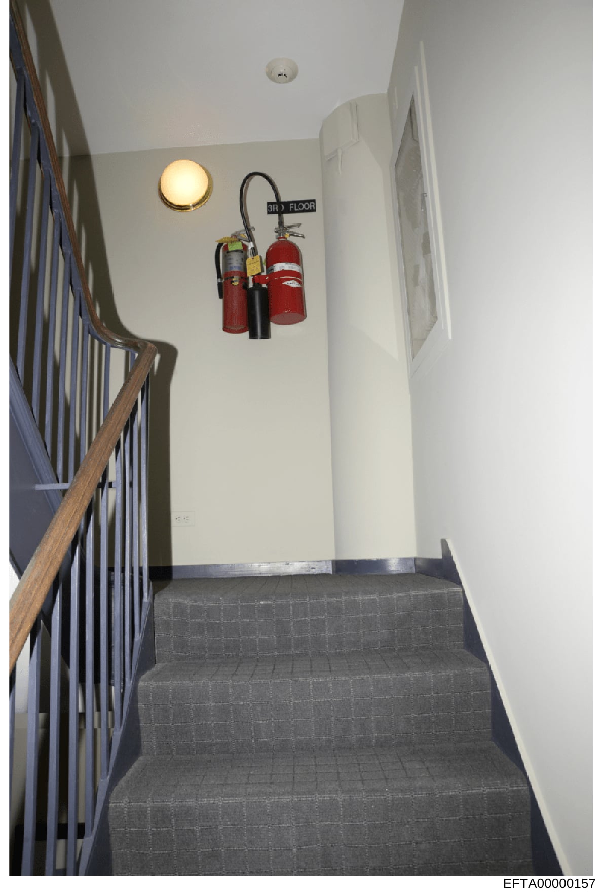 This is an evidence photograph showing the interior of a stairwell landing on the third floor of a building, featuring fire extinguishers and safety equipment mounted on the wall. The image documents the physical layout and safety infrastructure of w