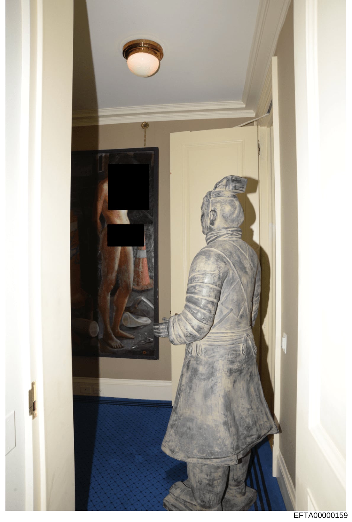 This photograph shows the interior of a residential hallway featuring a classical stone or plaster statue of a robed figure and a framed artwork depicting a partially nude male figure on the wall. The image captures the aesthetic and decor of what ap