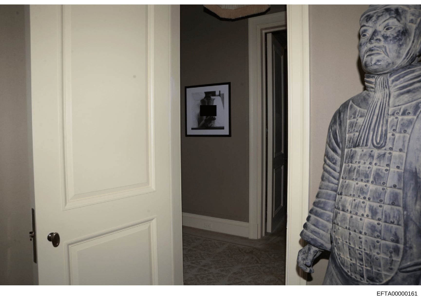 This is a photograph of an interior hallway in what appears to be a residential property, showing white-trimmed doorways, a gray accent wall with framed artwork, and a decorative blue and white ceramic or porcelain figure visible on the right side. T