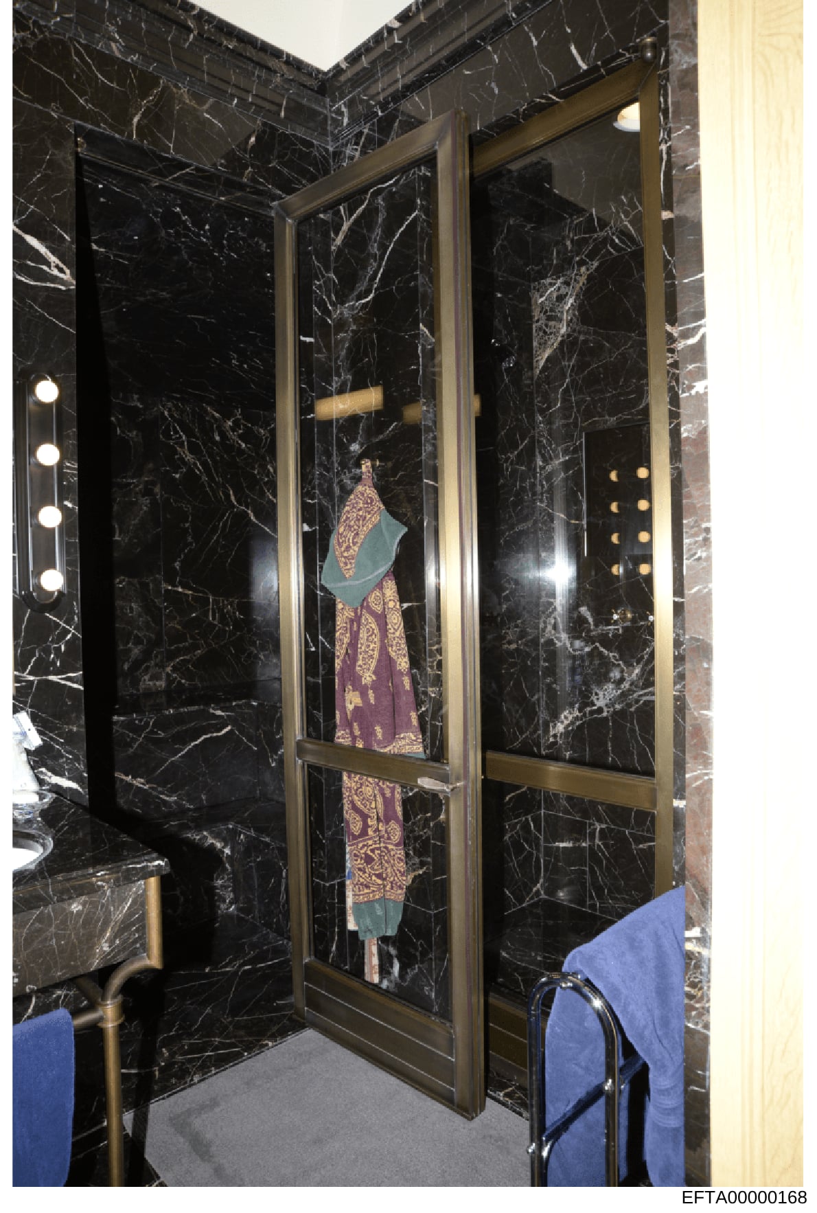 This evidence photograph shows a high-end bathroom interior featuring black marble walls with gold/brass fixtures and hardware. A garment (purple and patterned dress or robe with teal/green collar or wrap) is displayed on a hanger within a recessed n