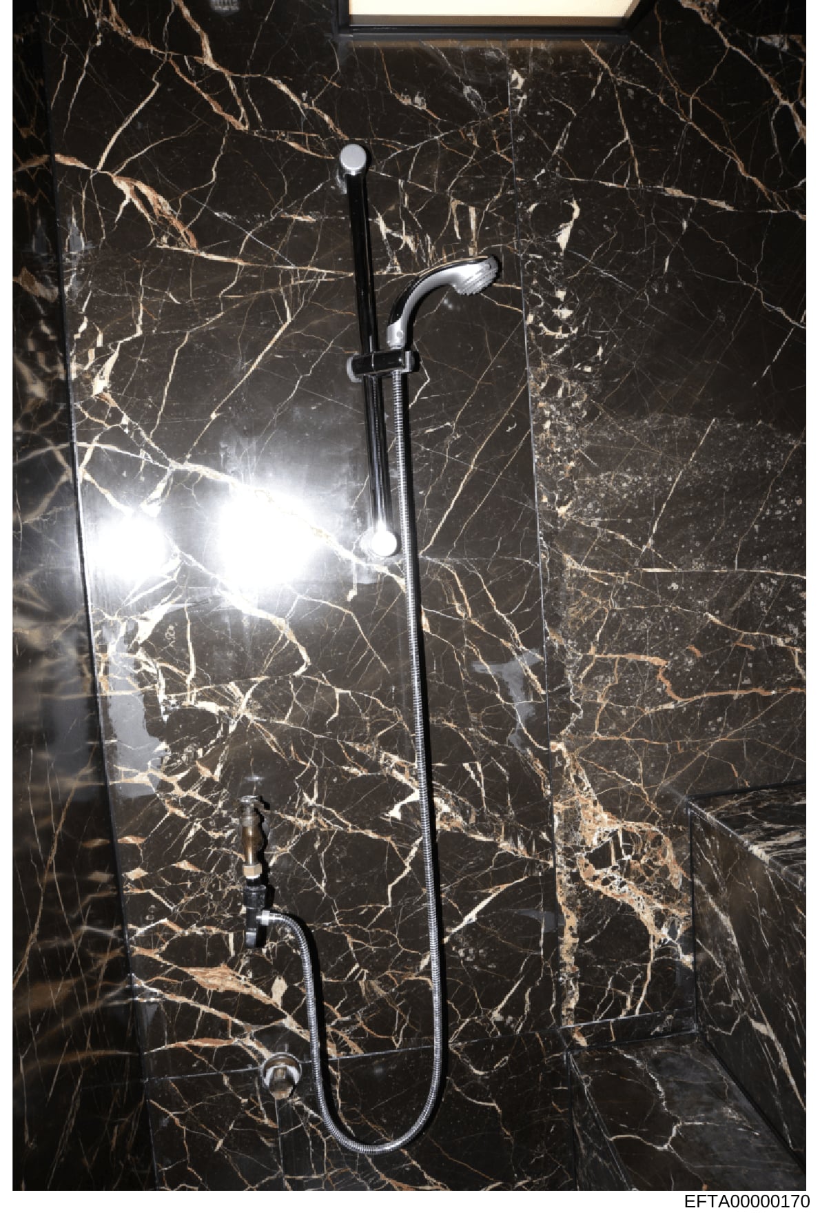 This is a photograph of a luxury bathroom shower installation, showing a contemporary chrome showerhead and handheld shower fixture mounted on black marble veined walls. The image appears to be evidence documentation from a property associated with t
