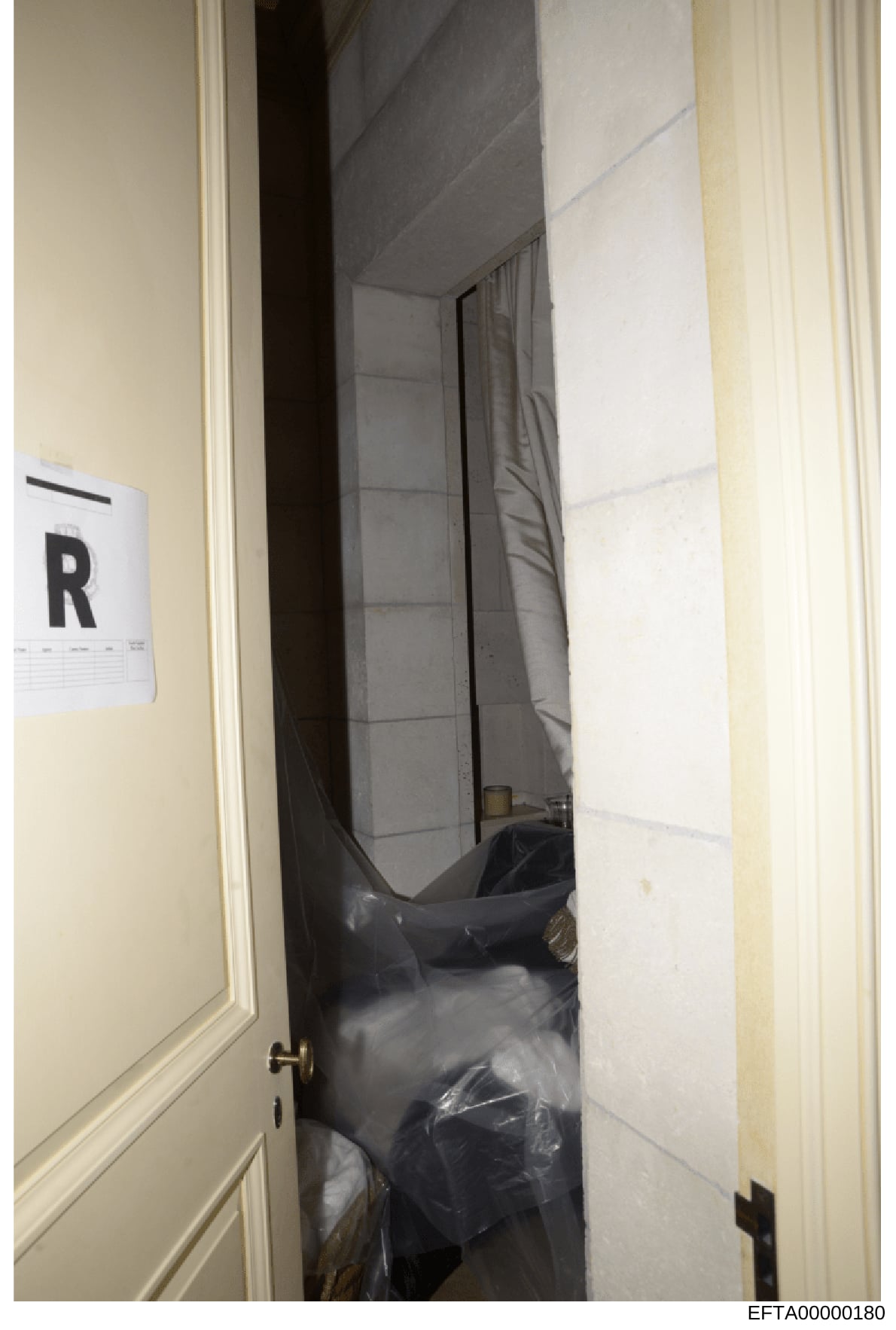 This is an evidence photograph showing an interior room or closet space with what appears to be furniture covered in dark plastic sheeting. An evidence marker labeled 'R' is visible on the wall, indicating this photo was taken during a forensic inves