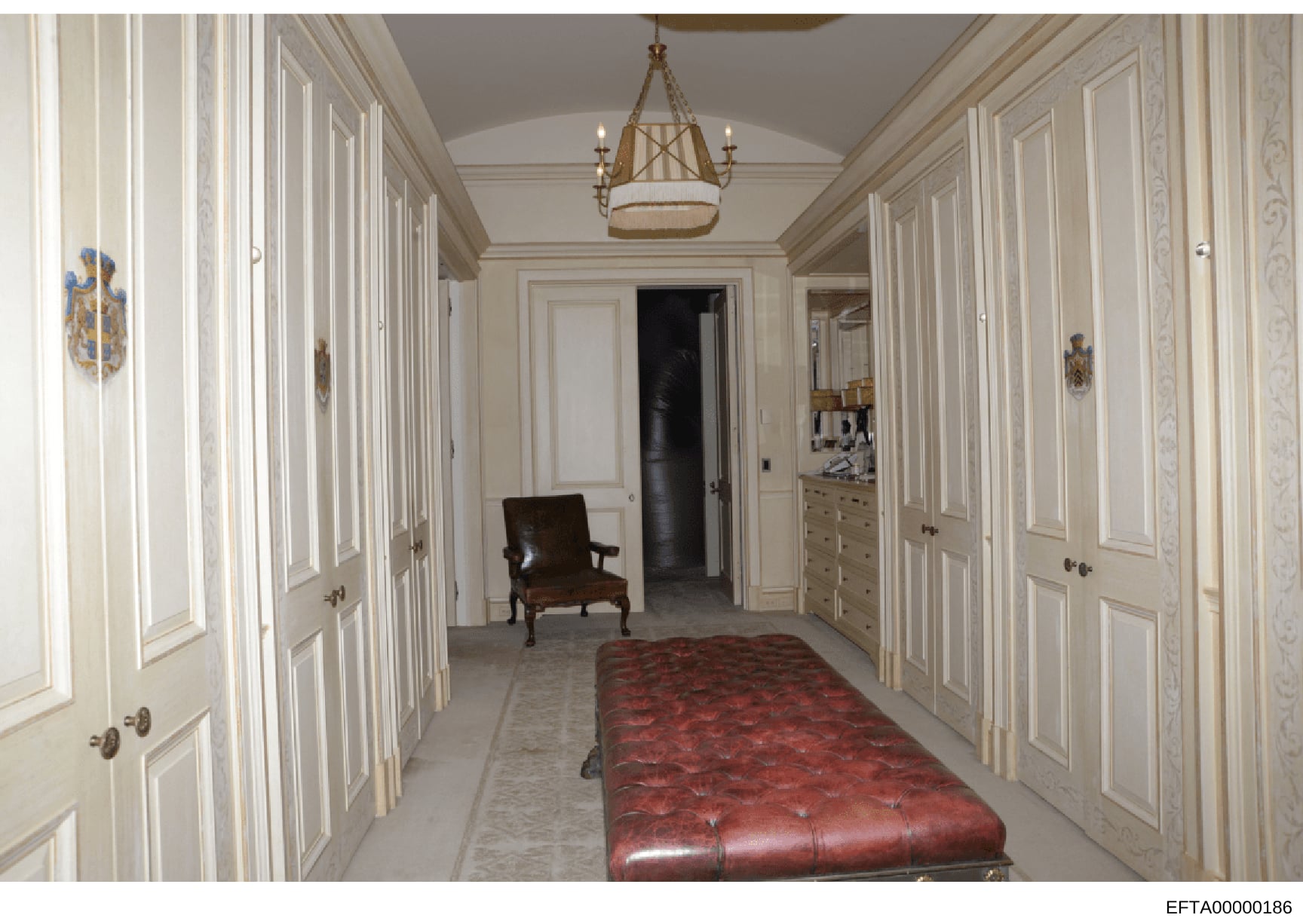 This is a photograph of a luxurious residential hallway featuring cream-colored paneled doors, a brass chandelier, ornate molding, and high-end furnishings. The image appears to be documentation of an interior space from one of Epstein's properties,
