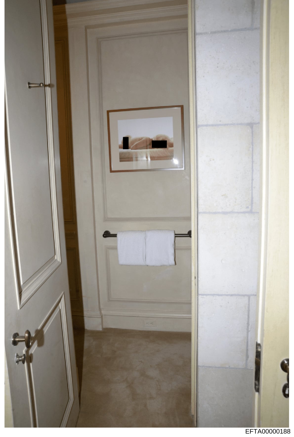 This is an evidence photograph of a bathroom interior, showing a framed artwork with censored/redacted figures, a towel rack with folded white towels, and white paneled walls. The image appears to be from a property inspection or evidence documentati