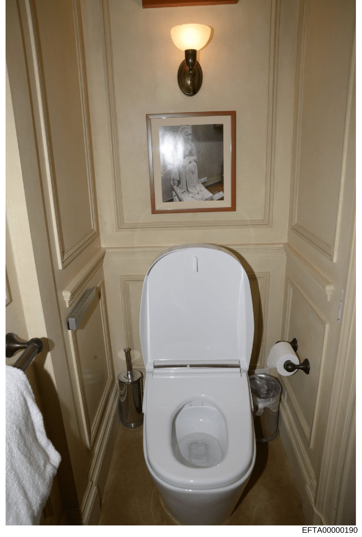 This is an evidence photograph showing a bathroom interior with a white toilet, wall sconces, framed artwork, and decorative fixtures. The image appears to be documentation of property interior spaces, likely taken during the investigation of one of
