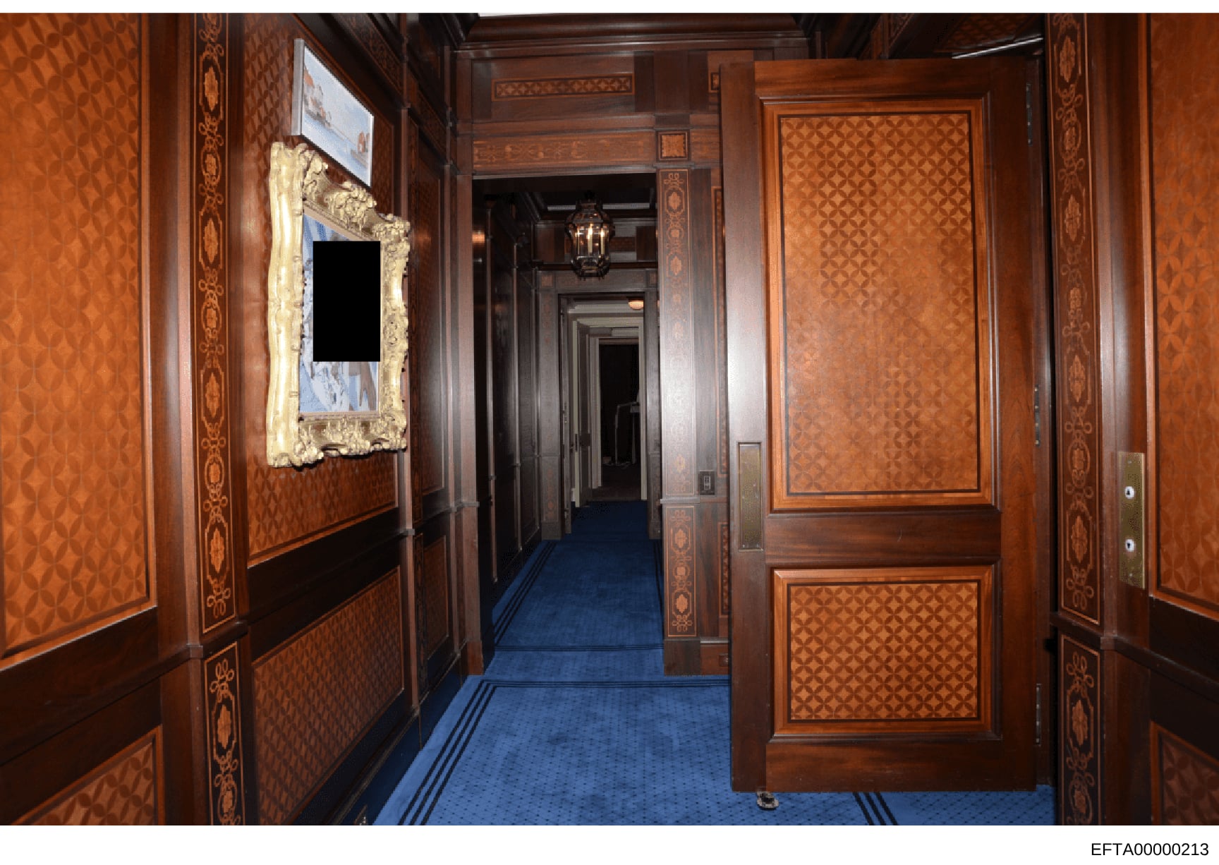This photograph shows a formal hallway inside one of Jeffrey Epstein's residences, featuring high-end wood paneling, inlaid decorative details, blue carpeting, and ornate furnishings. The image appears to be evidence documentation from the investigat
