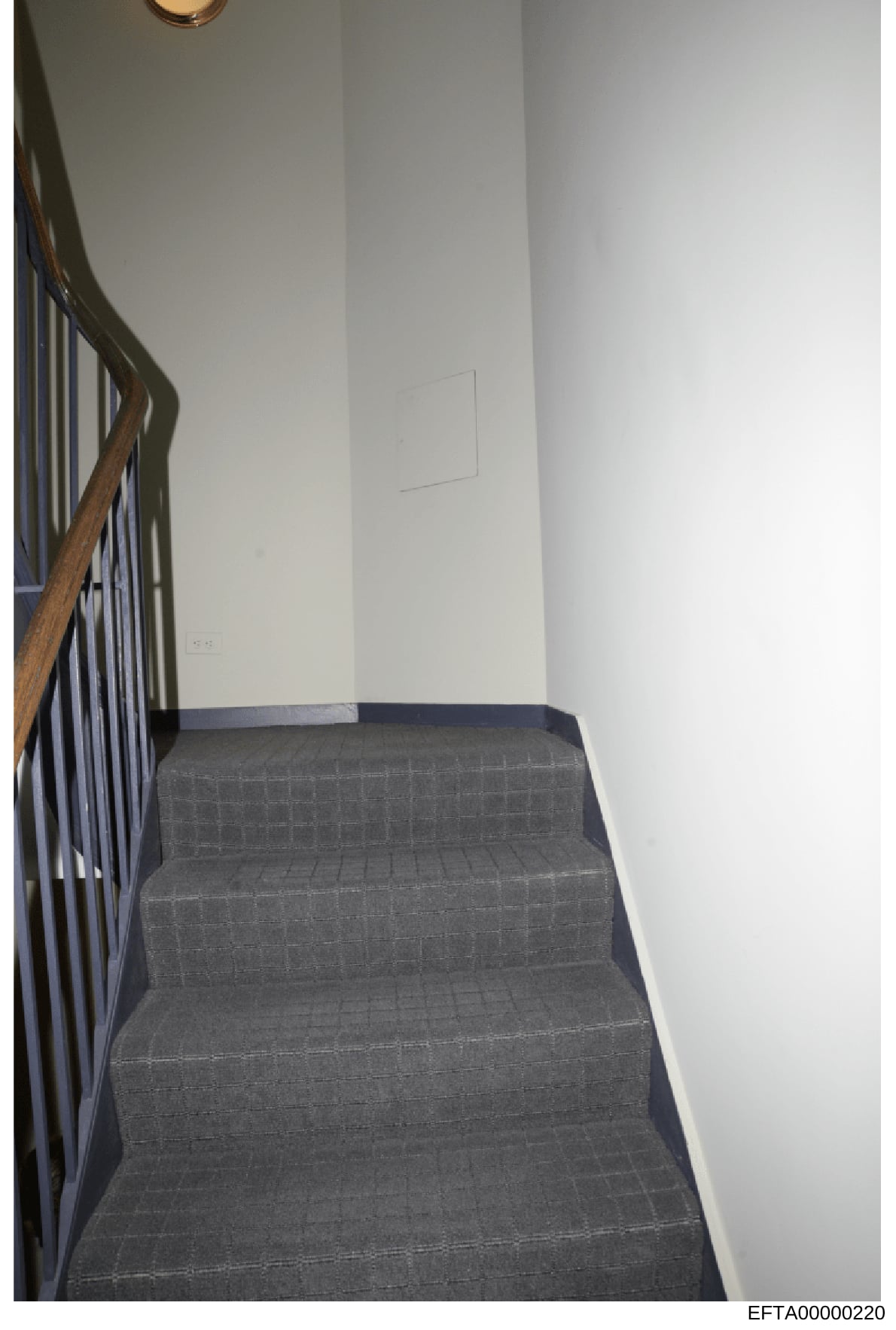 This is an evidence photograph showing an interior stairwell with gray carpeted steps and a wooden bannister on the left side. The stairwell features white walls, recessed lighting, and appears to be part of a residential property under investigation