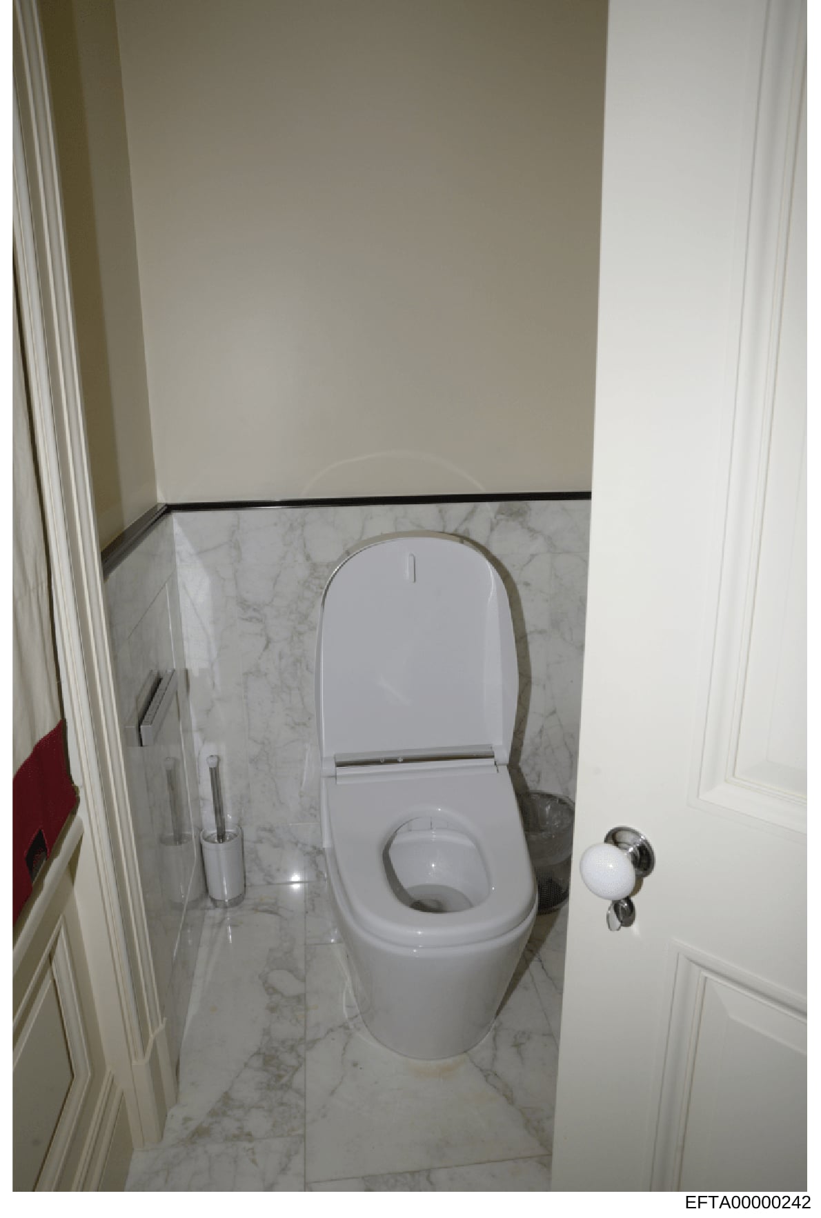 This is a photograph of a modern bathroom interior showing a white toilet with closed seat lid, marble flooring with gray veining, white painted walls, and stainless steel fixtures. The image appears to be documentation of property interior condition