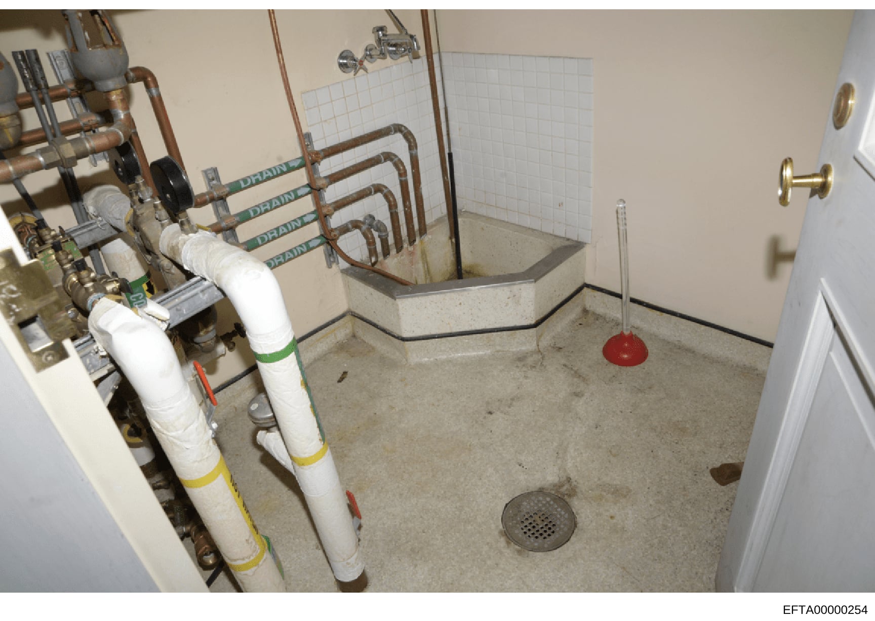 This is a photograph of a basement utility room showing plumbing infrastructure including water filtration systems, drain pipes, and a floor drain. The image appears to be evidence documentation from the investigation, likely taken at one of Epstein'