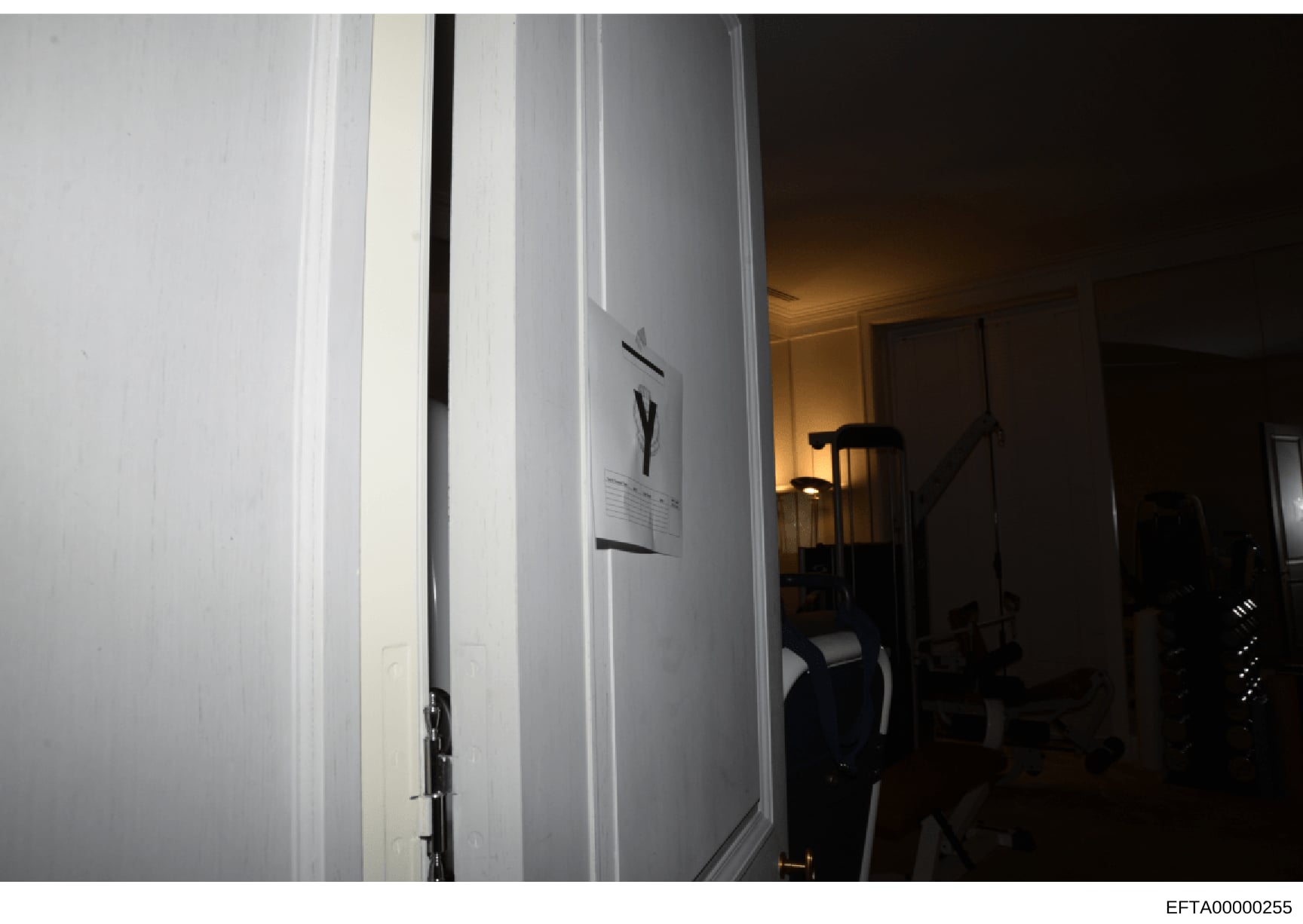 This is an evidence photograph taken during an investigation, showing an interior hallway or passage area with white walls, doorways, and minimal furnishings. The image appears to be part of a property search or documentation of a residential or comm