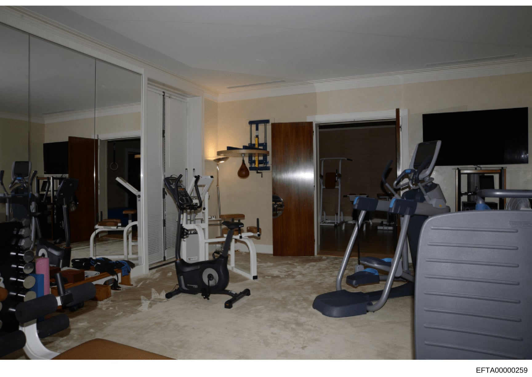 This photograph shows a professionally equipped home gym space within what appears to be a luxury residence. The room contains multiple exercise machines including stationary bikes, elliptical equipment, and weight training apparatus, along with mirr