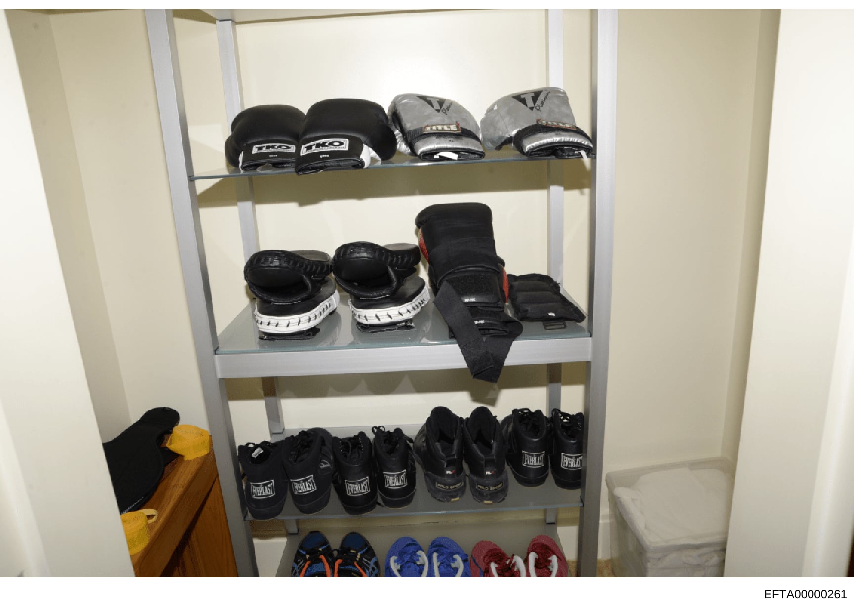 This is a forensic evidence photograph showing a shelving unit containing various boxing gloves, hand wraps, and athletic footwear. The image captures multiple pairs of boxing gloves in black and gray colorways (including brands like Everlast and TKO