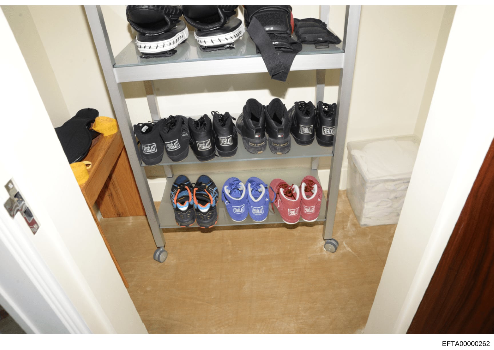 This is an evidence photograph showing a metal shelving unit containing multiple pairs of athletic shoes and boxing equipment, including Everlast-branded boxing boots in various colors (black, blue, red) and what appears to be boxing gloves or protec