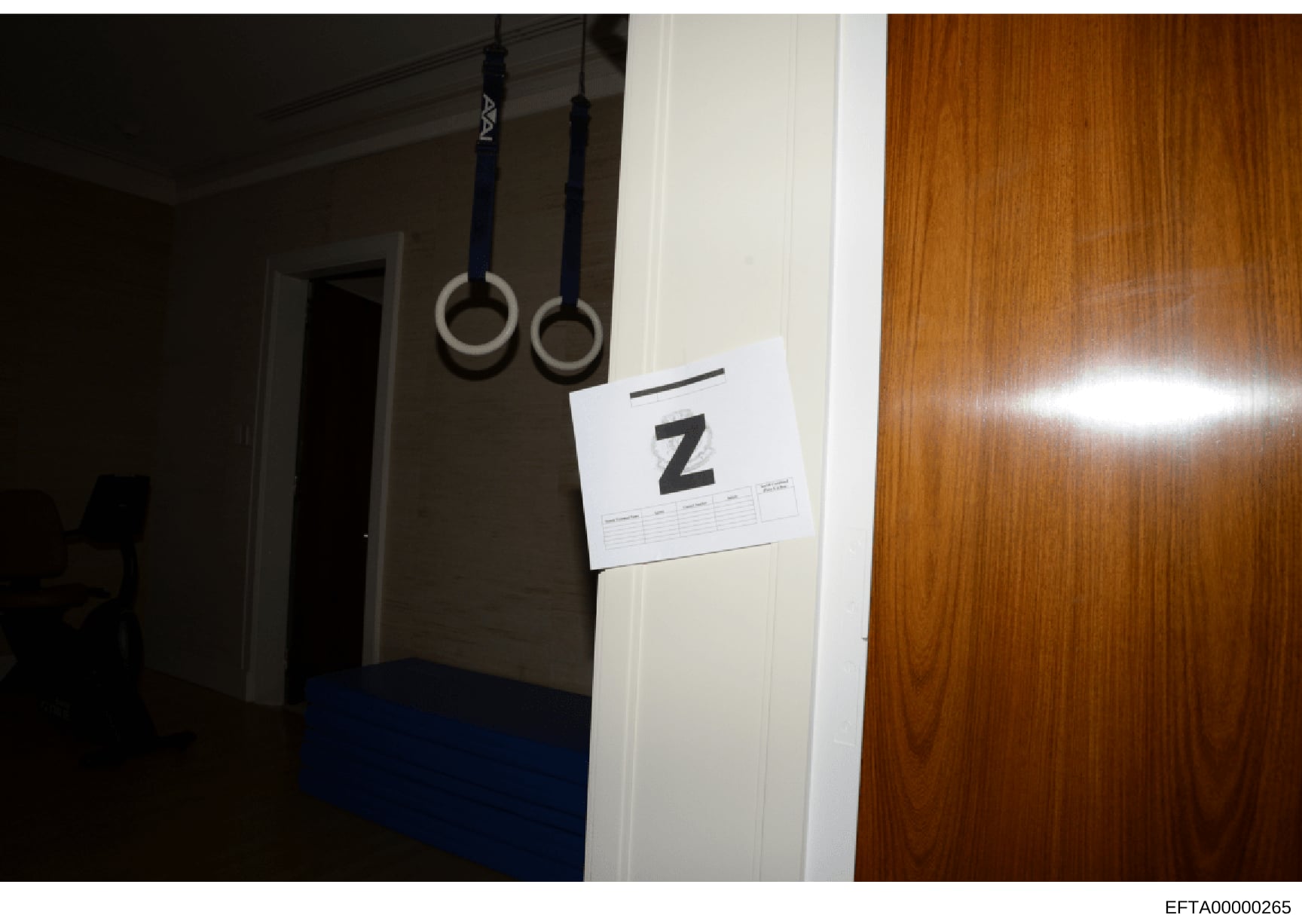 This is an evidence photograph from an FBI or law enforcement search, showing an interior room with gymnastics rings suspended from the ceiling and a white evidence marker labeled 'Z'. The marker indicates the location and item numbering for forensic