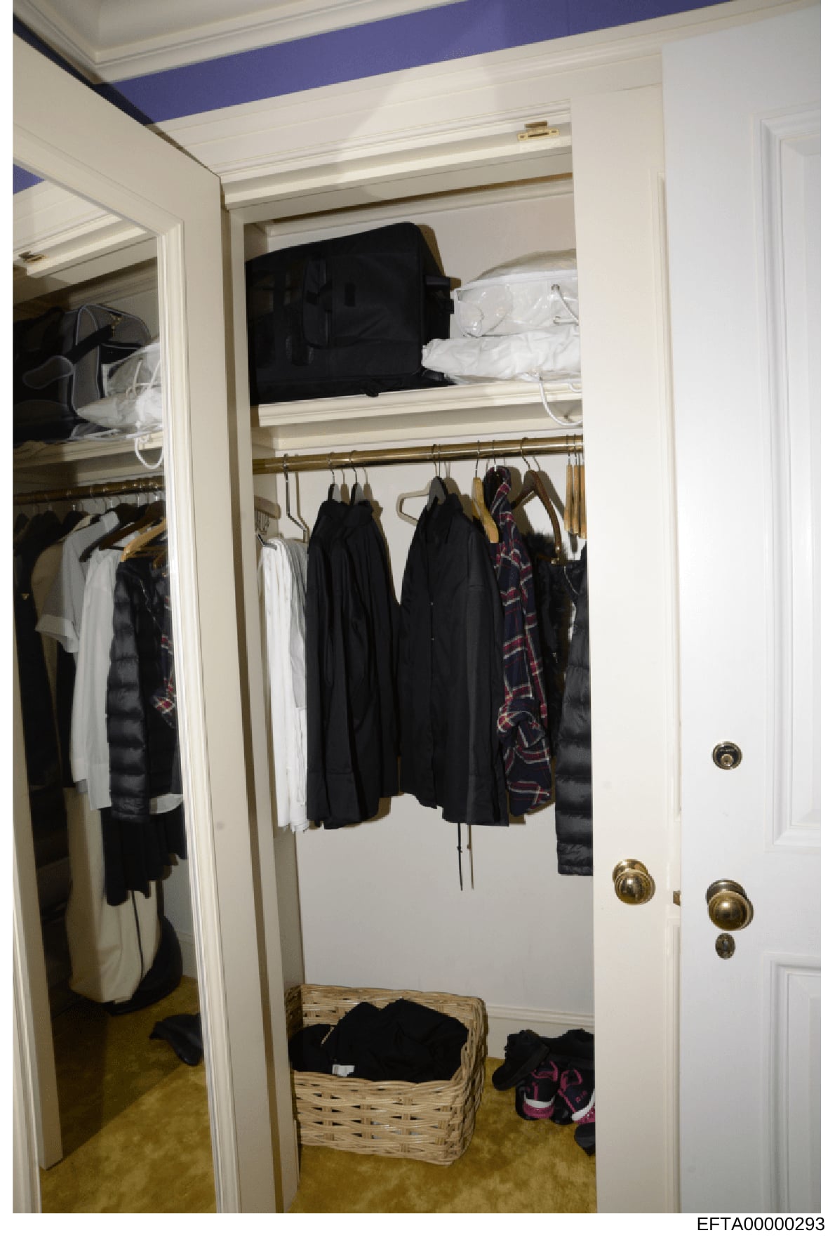 This is a photograph of a residential walk-in closet showing organized clothing storage, including hanging garments, shelved items, and a wicker basket with shoes. The closet features white finishes, brass hardware, and a blue accent stripe on the ce