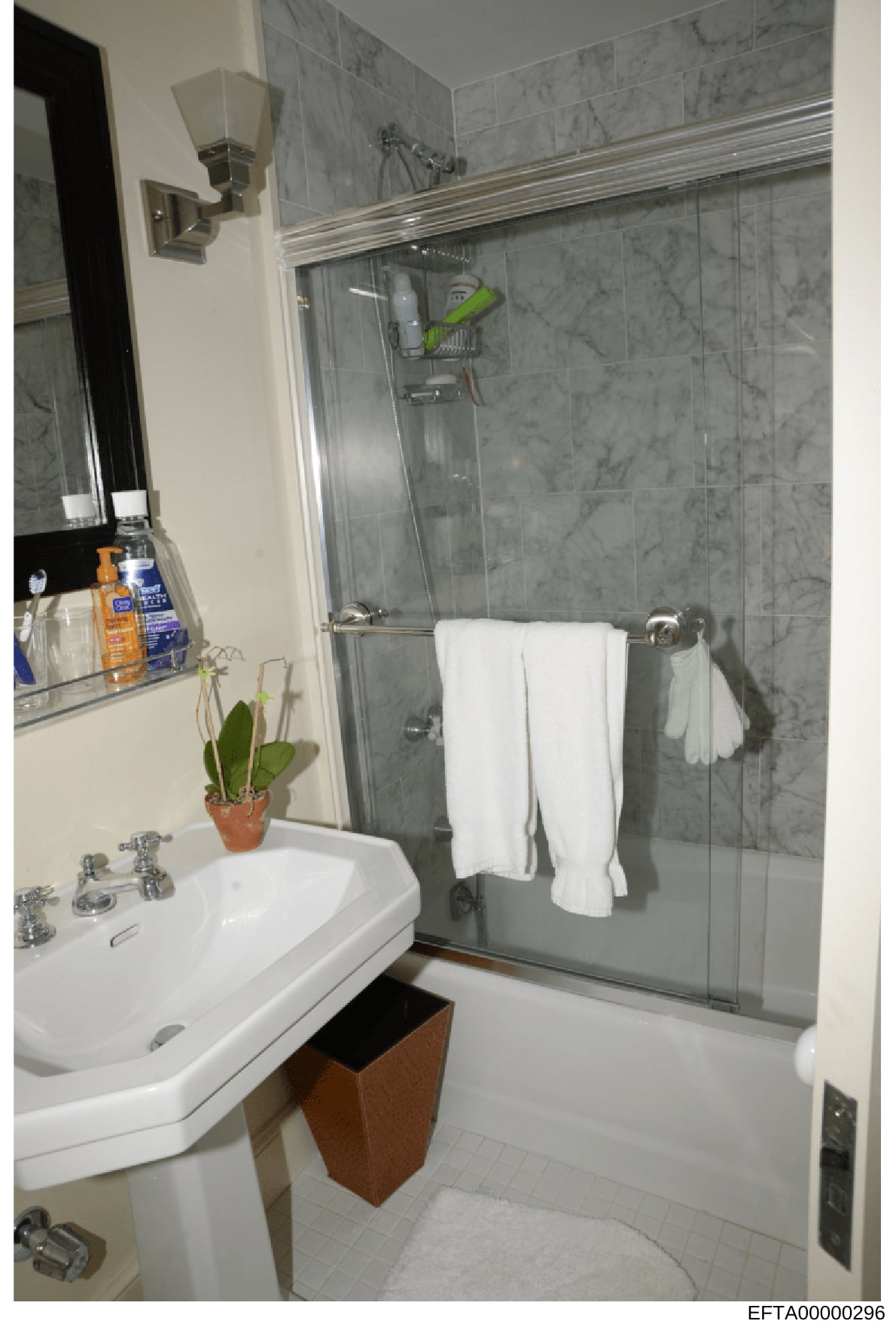 This is a photograph of a modern bathroom interior, showing a white pedestal sink, glass-enclosed shower with gray marble tile, mirror, towel racks, and bathroom amenities. The image appears to be documentation of a residential property, likely from