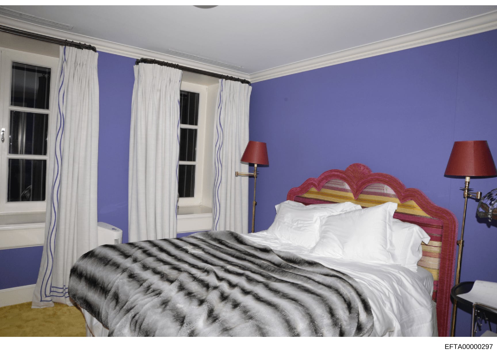 This is a photograph of a residential bedroom interior, featuring bold purple walls, a red ornate headboard, white linens, and coordinating furnishings. The image appears to be documentation of interior design or property contents, likely taken as pa