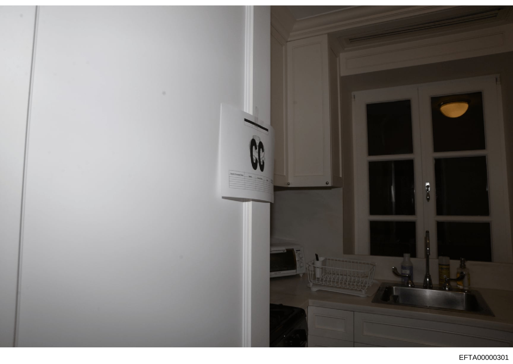 This photograph shows an interior kitchen space with modern white appliances, cabinetry, and a window with glass doors. The image appears to be documentation of a residential property, likely taken as part of an evidence collection or property invent