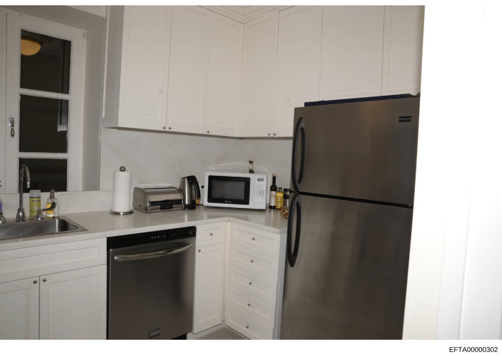 A photograph of a modern residential kitchen featuring white cabinetry, stainless steel appliances, and contemporary finishes. The image shows the kitchen layout and contents, likely taken as part of property documentation or evidence photography in 