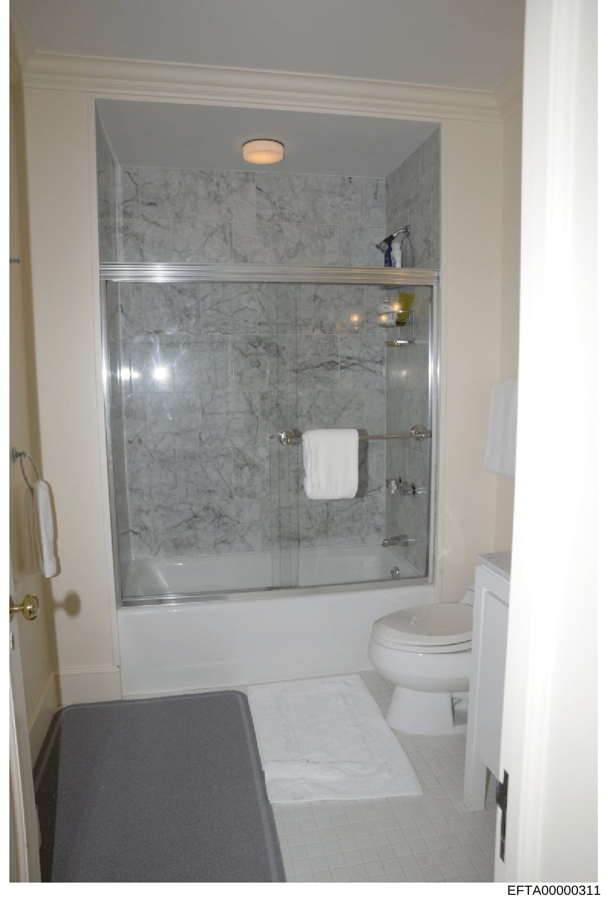 This photograph depicts a residential bathroom featuring a marble-tiled shower enclosure with glass doors, a white toilet, and white tile flooring. The image appears to be documentation of property interiors, potentially related to one of Epstein's r