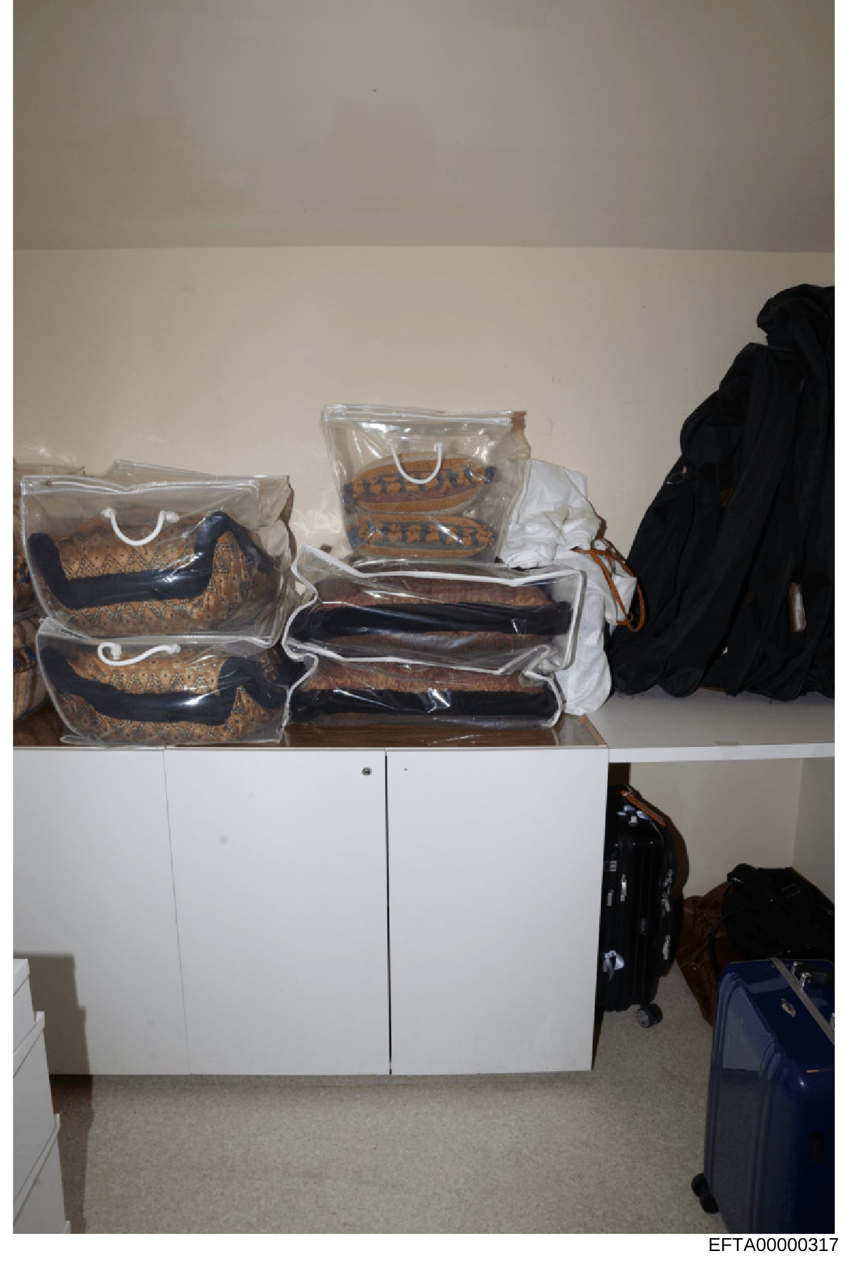 This is a photograph of the interior of a residential closet or storage area showing multiple designer handbags in clear protective storage bags arranged on top of a white cabinet, along with black and dark-colored clothing items. The photo appears t