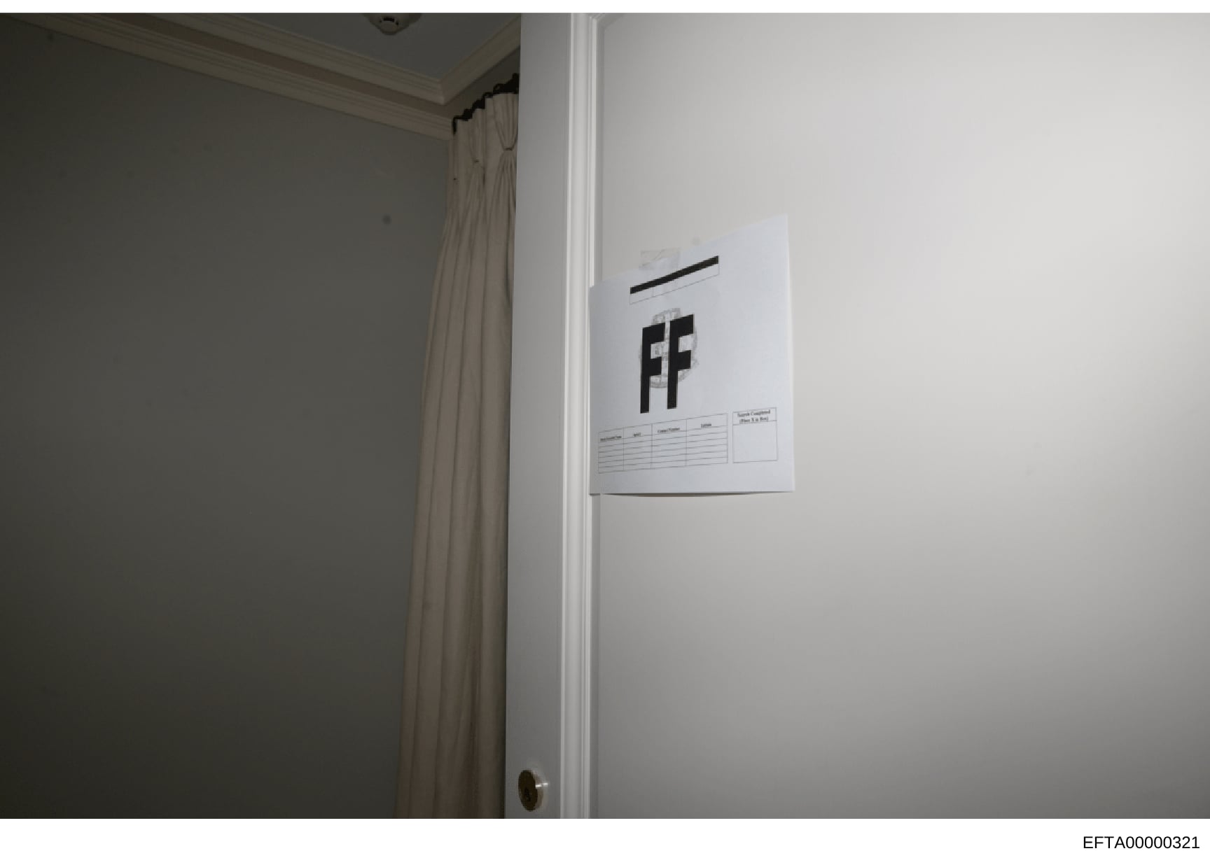 This is an evidence photograph showing the interior of a room with a white document or sign affixed to a white wall. The document displays the letters 'FF' prominently and appears to have a reference grid or measurement scale at the bottom, consisten