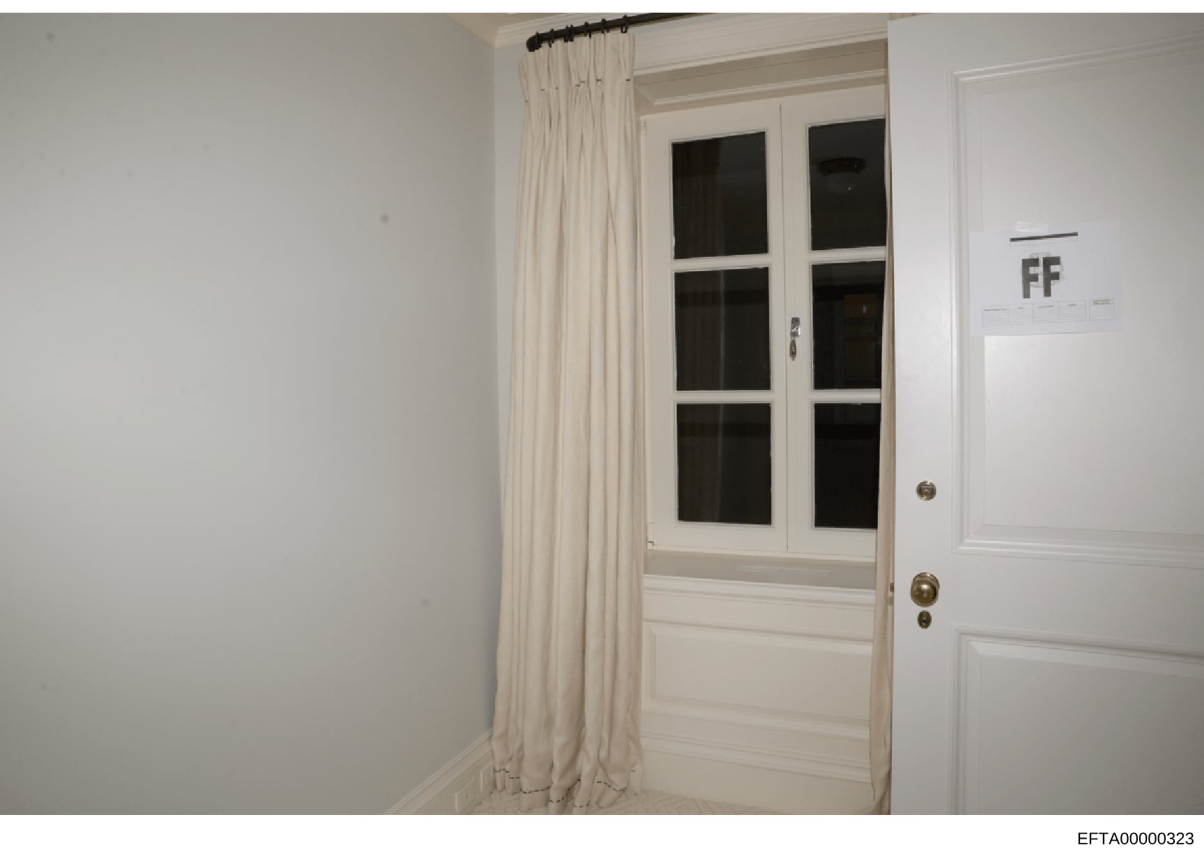 This is an evidence photograph showing the interior of a room with a white wooden door featuring six glass panes, white walls, and cream-colored curtains. The image appears to be from a property inspection or evidence documentation related to the inv