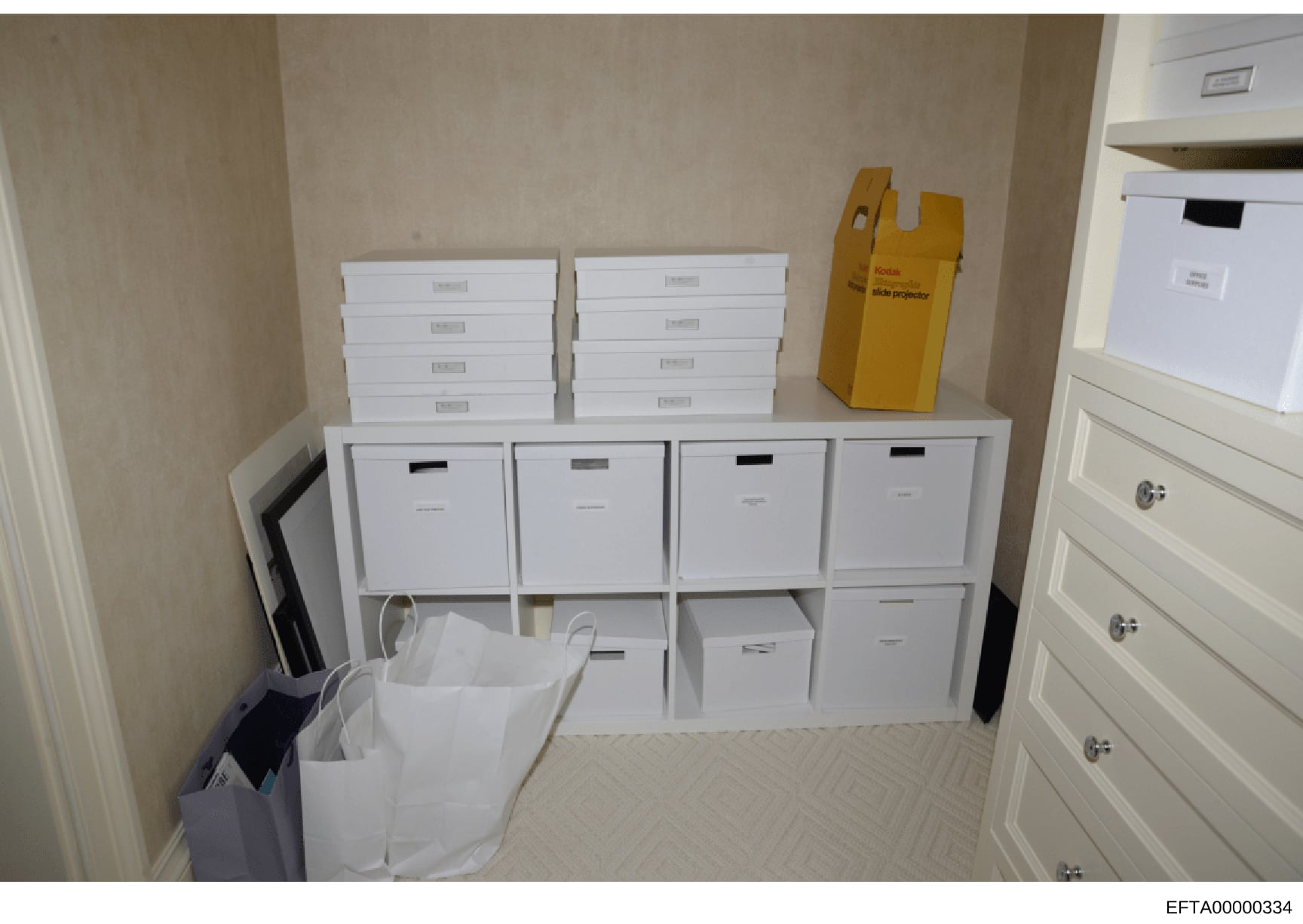 This photograph documents the interior of a storage closet or room containing numerous white filing boxes organized on shelving units, along with a yellow Kodak slide projector and other office equipment. The image appears to be evidence documentatio