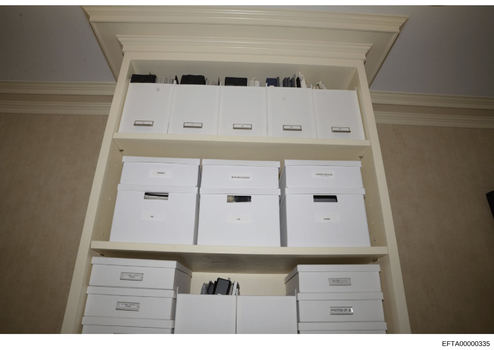 This photograph documents a built-in storage cabinet containing multiple white boxes and file folders, each labeled with identification tags or labels. The boxes appear to be organized evidence storage, likely part of law enforcement documentation an