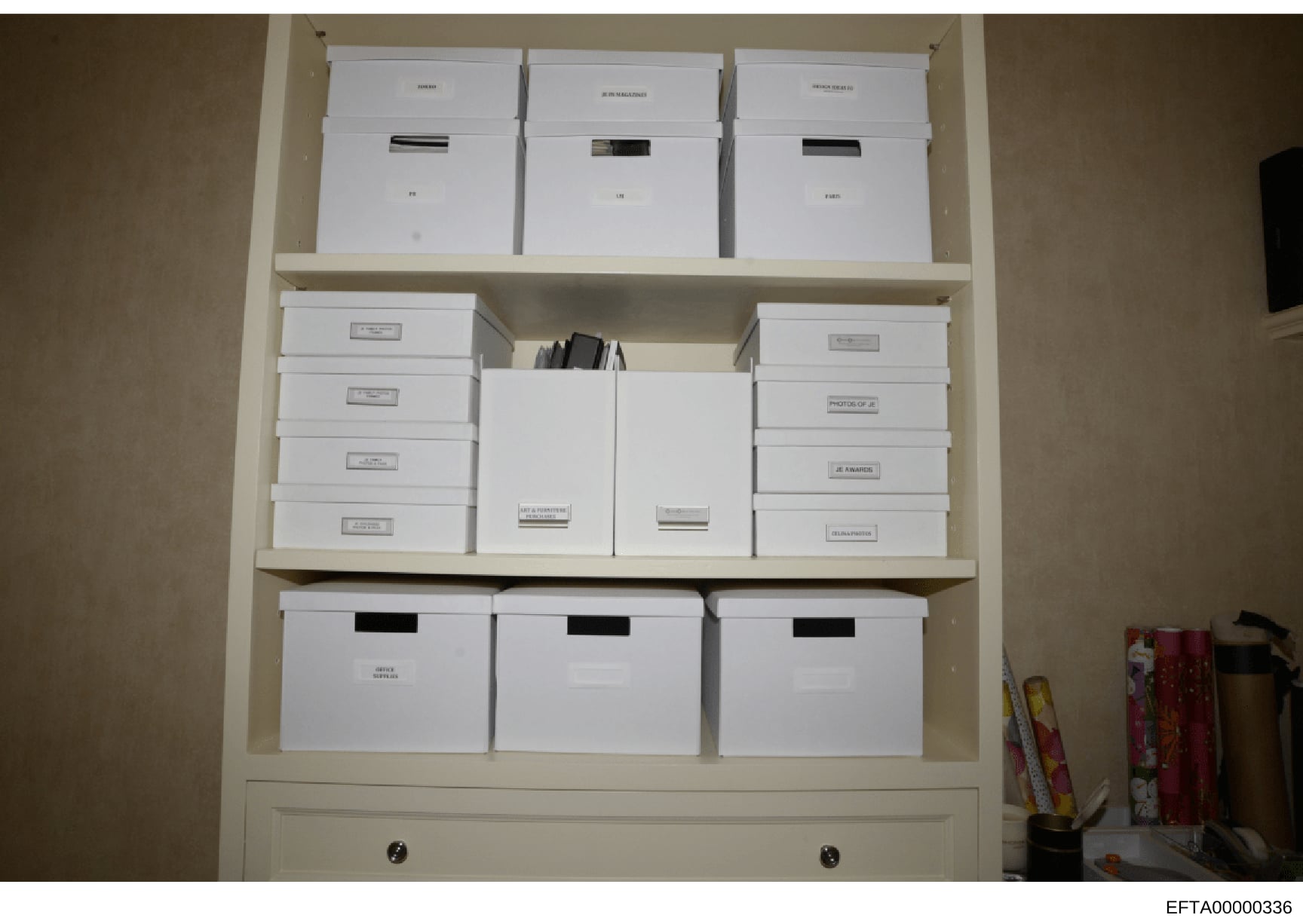 This is an evidence photograph showing a built-in shelving unit containing multiple white storage boxes with various labels and redactions. The boxes appear to be organized evidence or documents related to the investigation, with some labels visible 