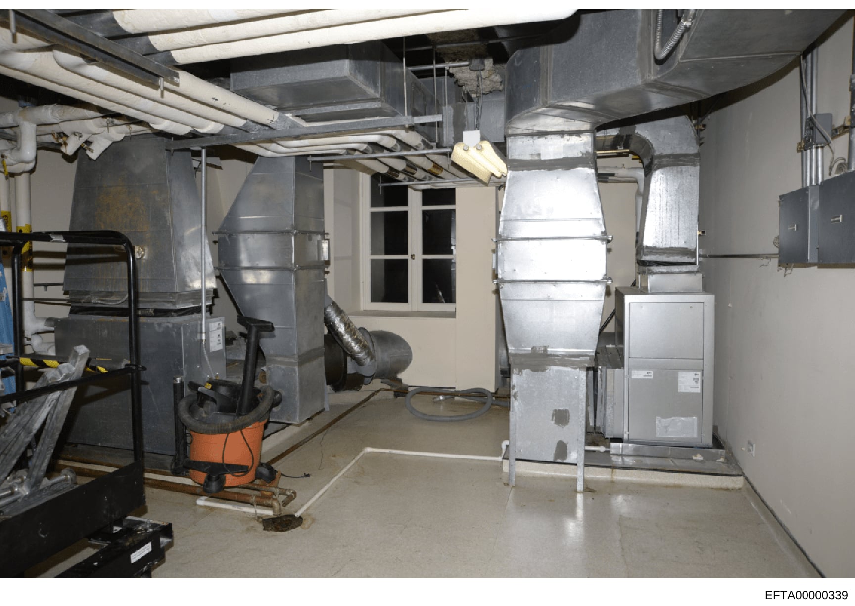 This is a photograph of a basement mechanical/utility room showing HVAC systems, ductwork, piping, and related building infrastructure. The image documents the mechanical systems and basement conditions of a property under investigation, likely taken